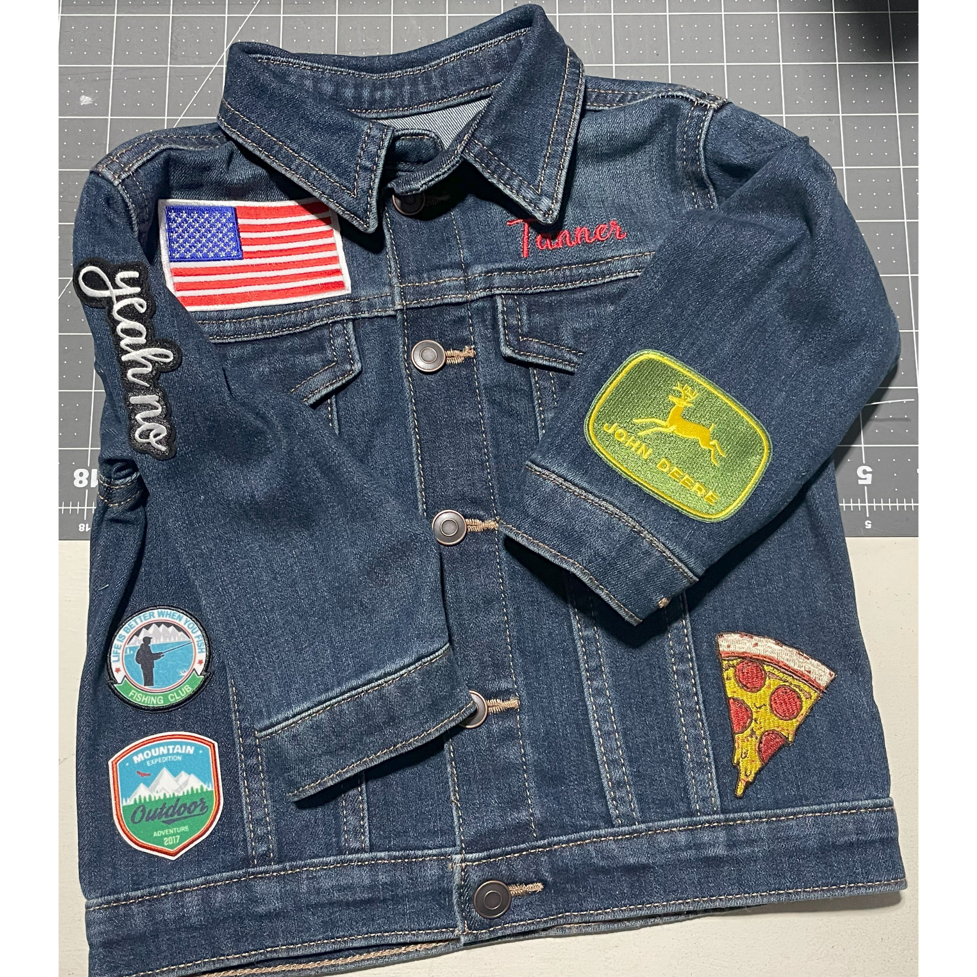 Denim jacket covered with colorful patches, including an American flag and a pizza slice, on a gray background