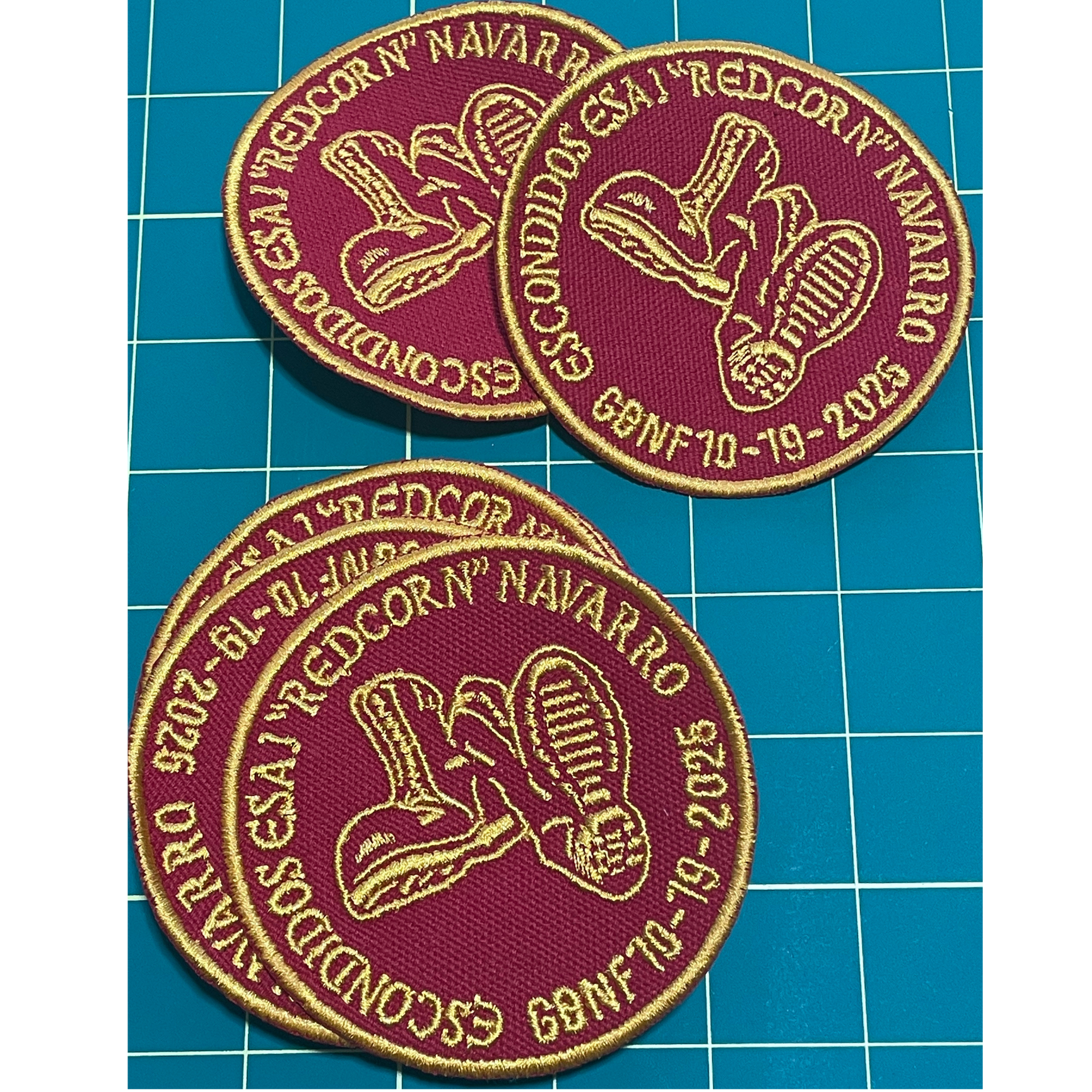 Two maroon embroidered patches with gold border and text on a blue grid background