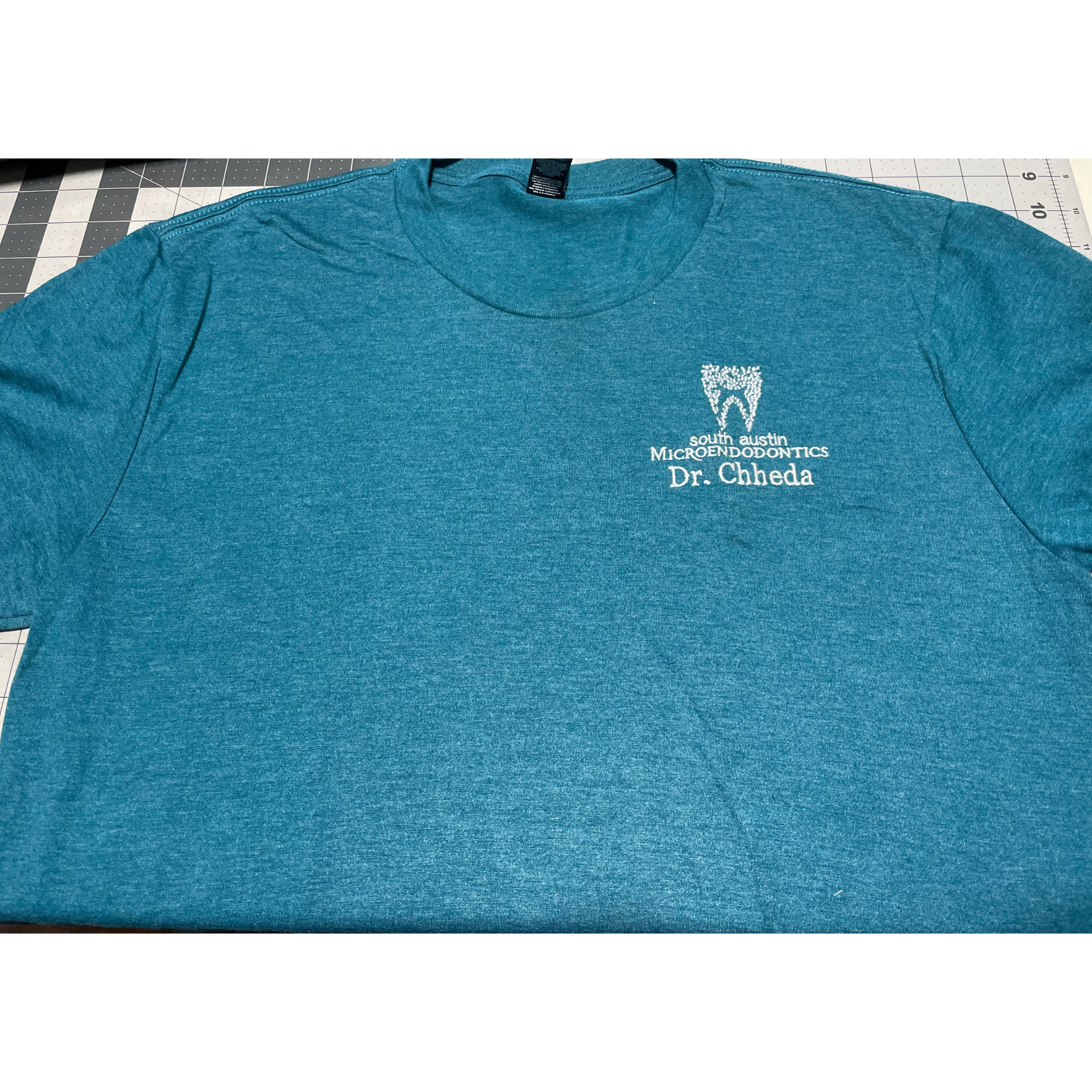 Teal heather T-shirt with small white chest logo on a flat surface
