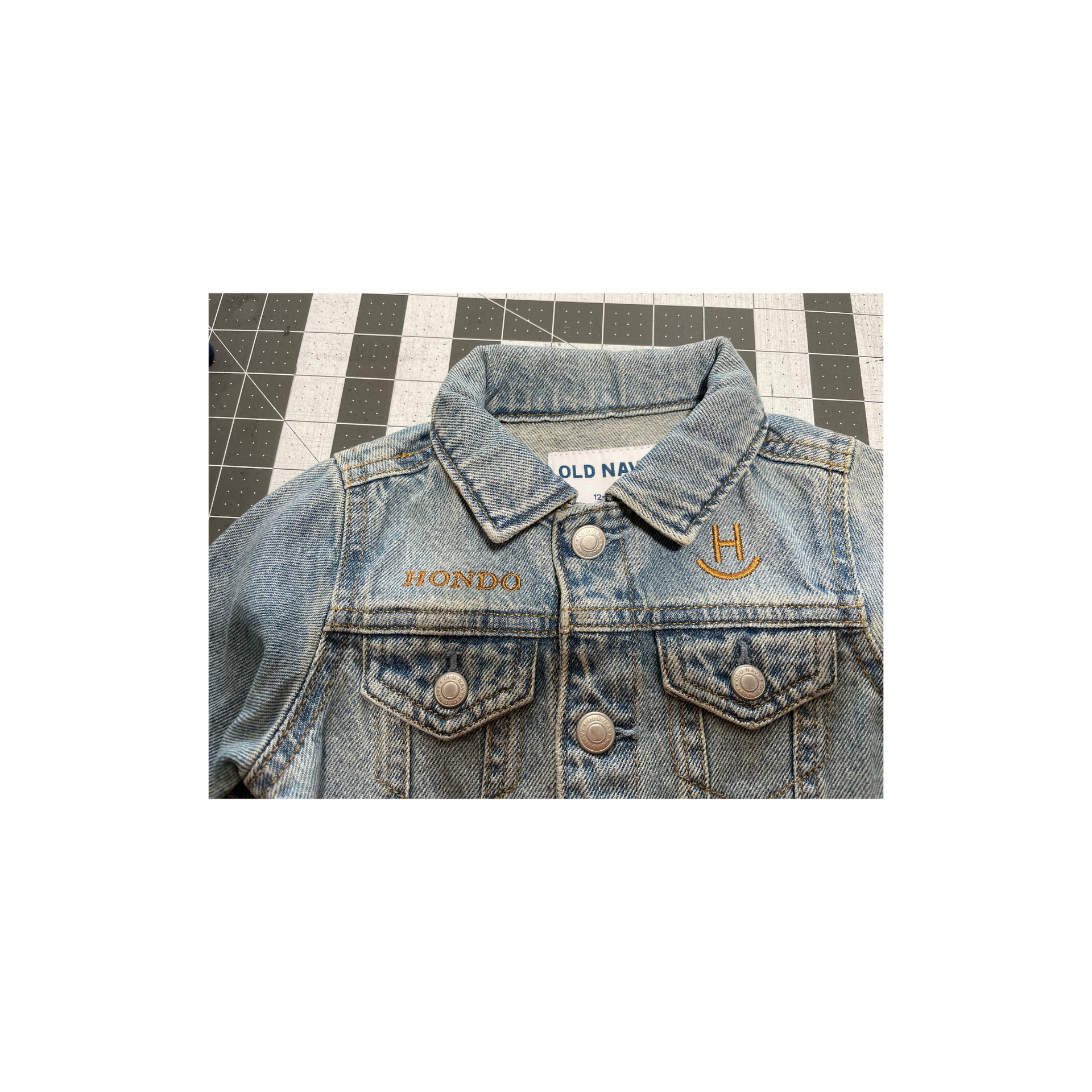Denim jacket laid flat on striped floor, showing collar, buttons, and chest pockets.