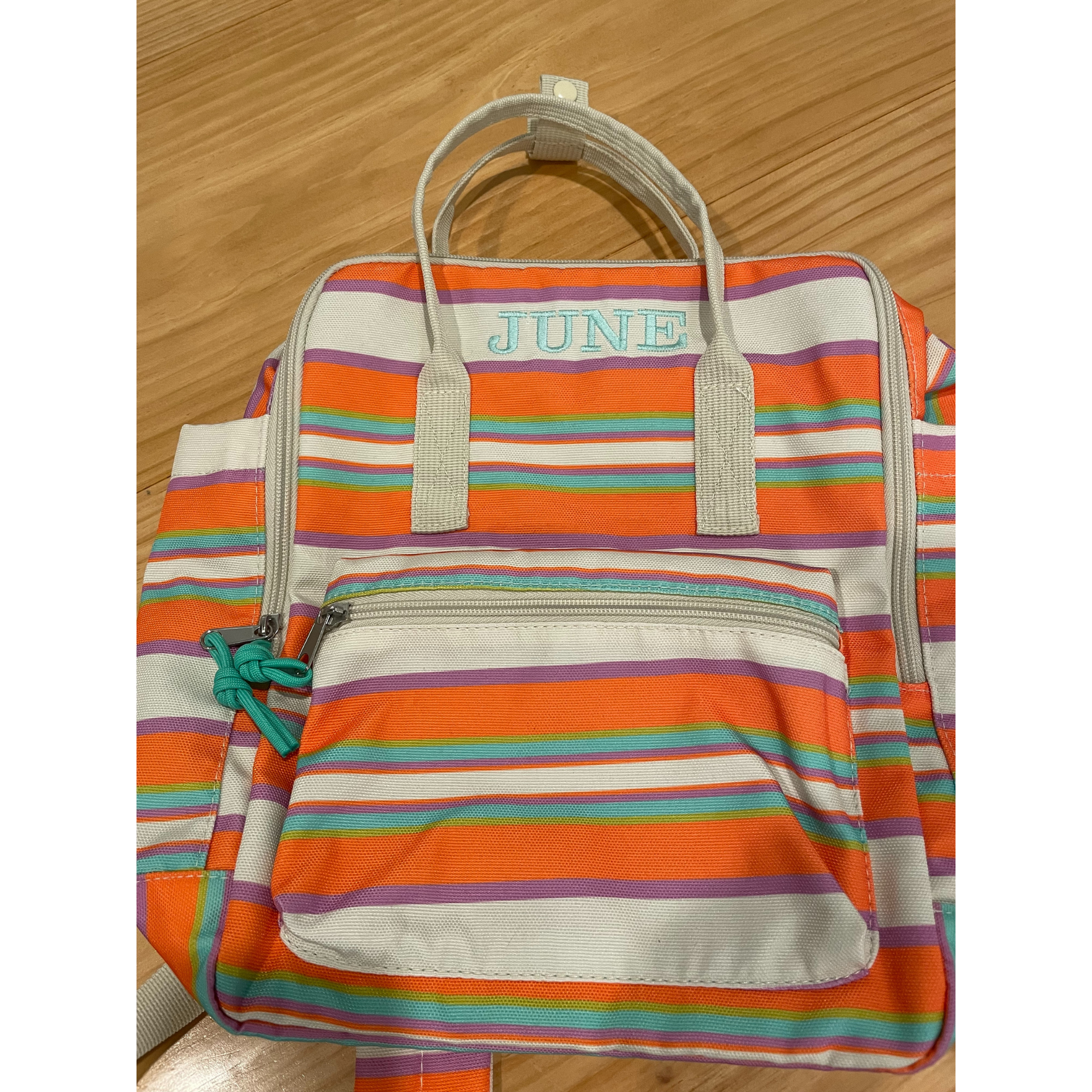 Colorful striped backpack with beige handles and front pocket on a wooden surface