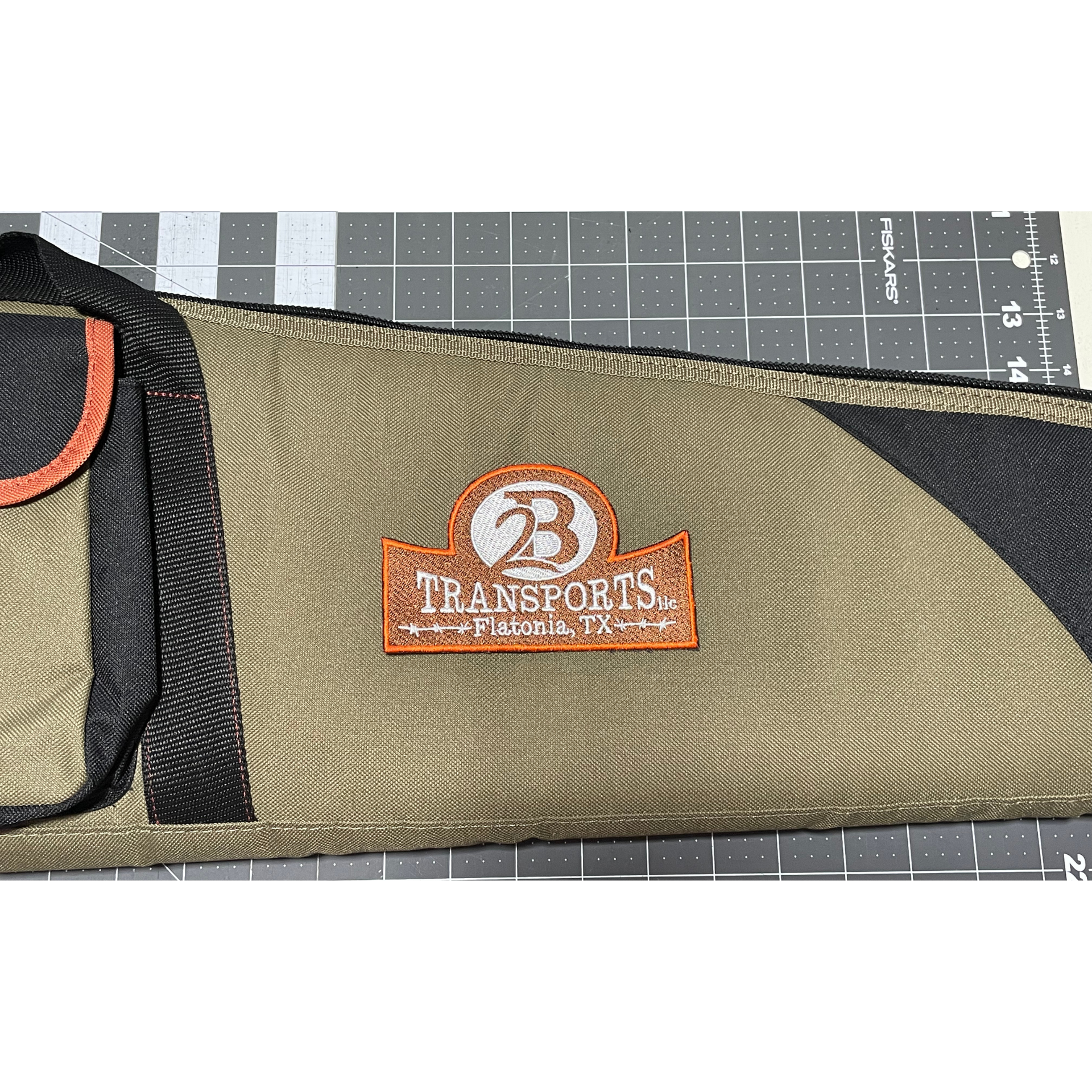 Olive and black fabric pouch with orange “73 TRANSFERS” logo on a cutting mat