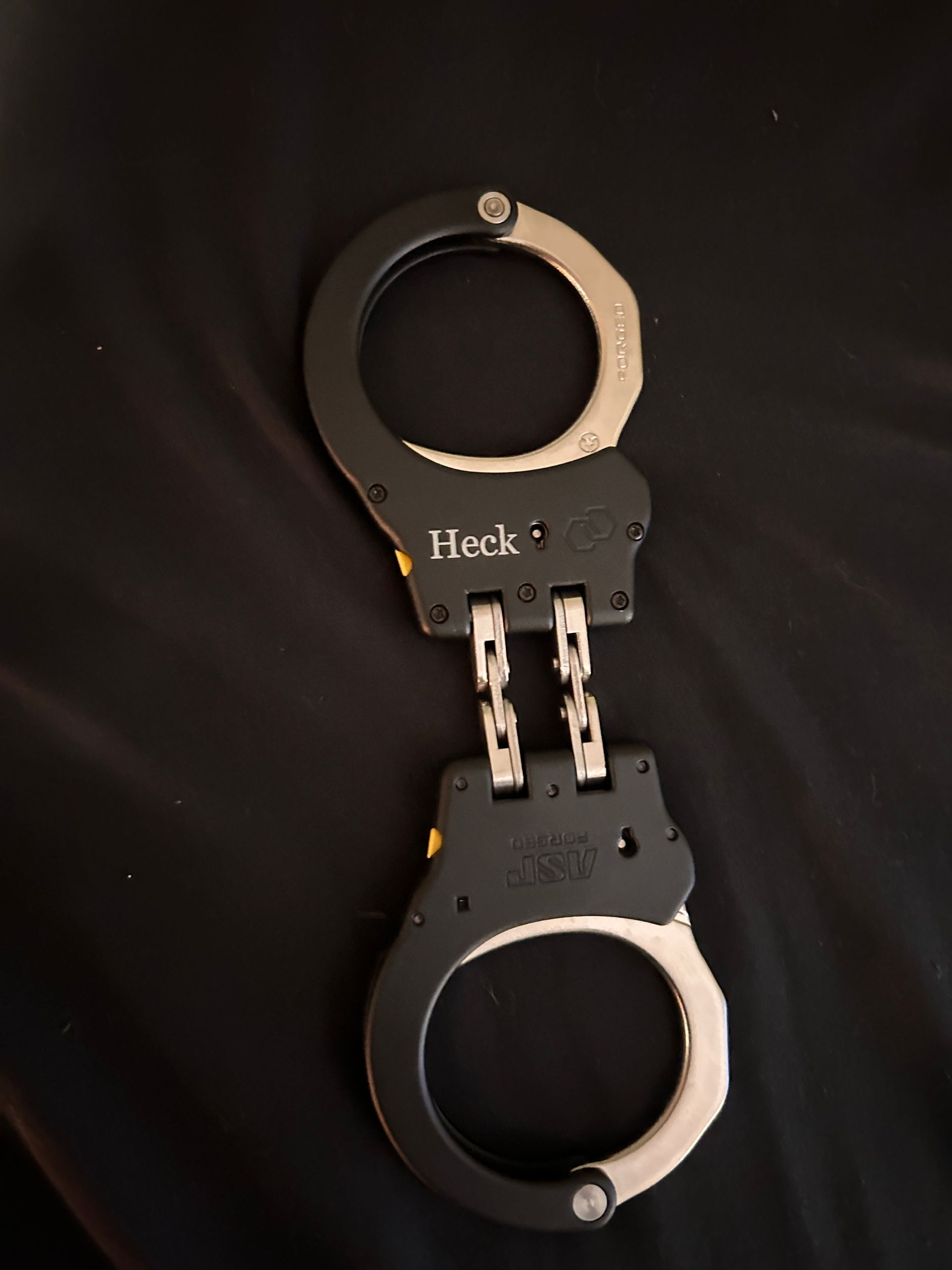 Black metal handcuffs with silver rings, shown on a dark background.