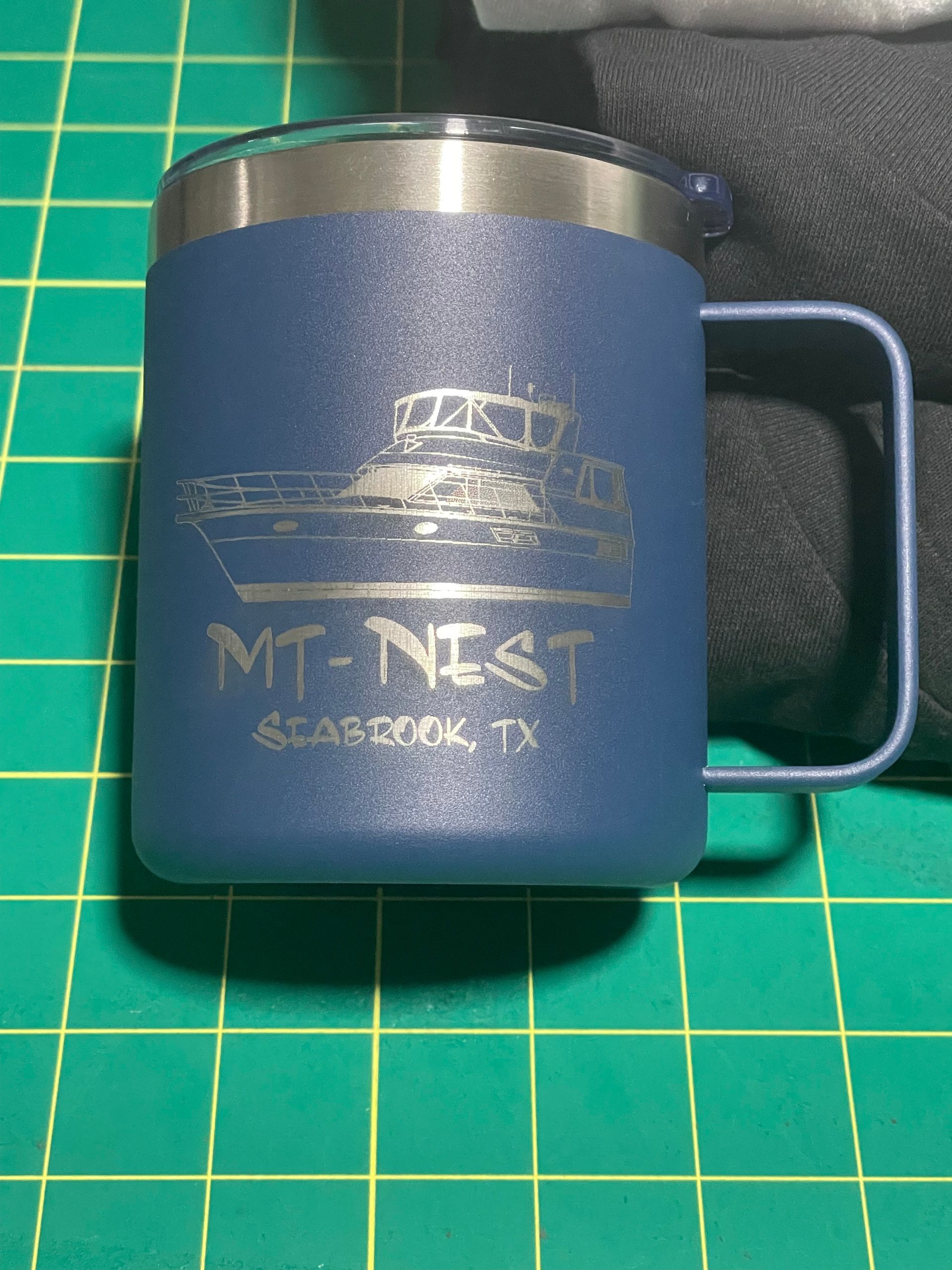 Blue insulated mug with silver lid and handle on a green cutting mat, labeled “MT NEST” and “Birmingham.”