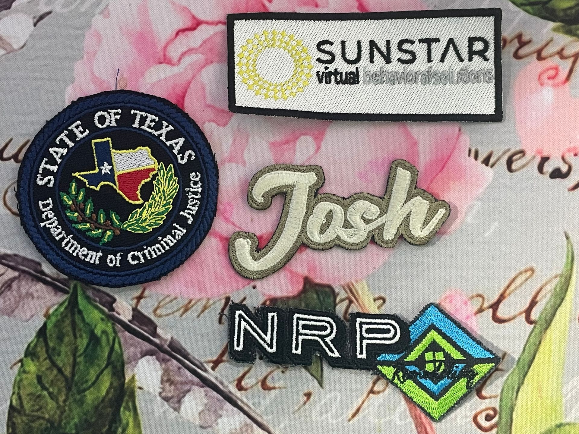 Patches and name tags on a pink cursive fabric background, including “Josh,” SUNSTAR, and Texas State Board of Cosmetology.