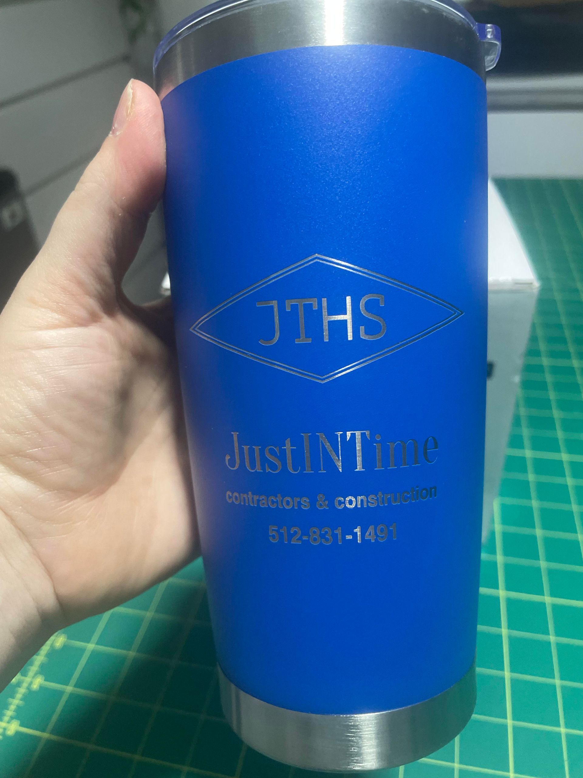 Blue insulated tumbler with silver lid and base, featuring “JTHS justinTime” logo held in a hand.