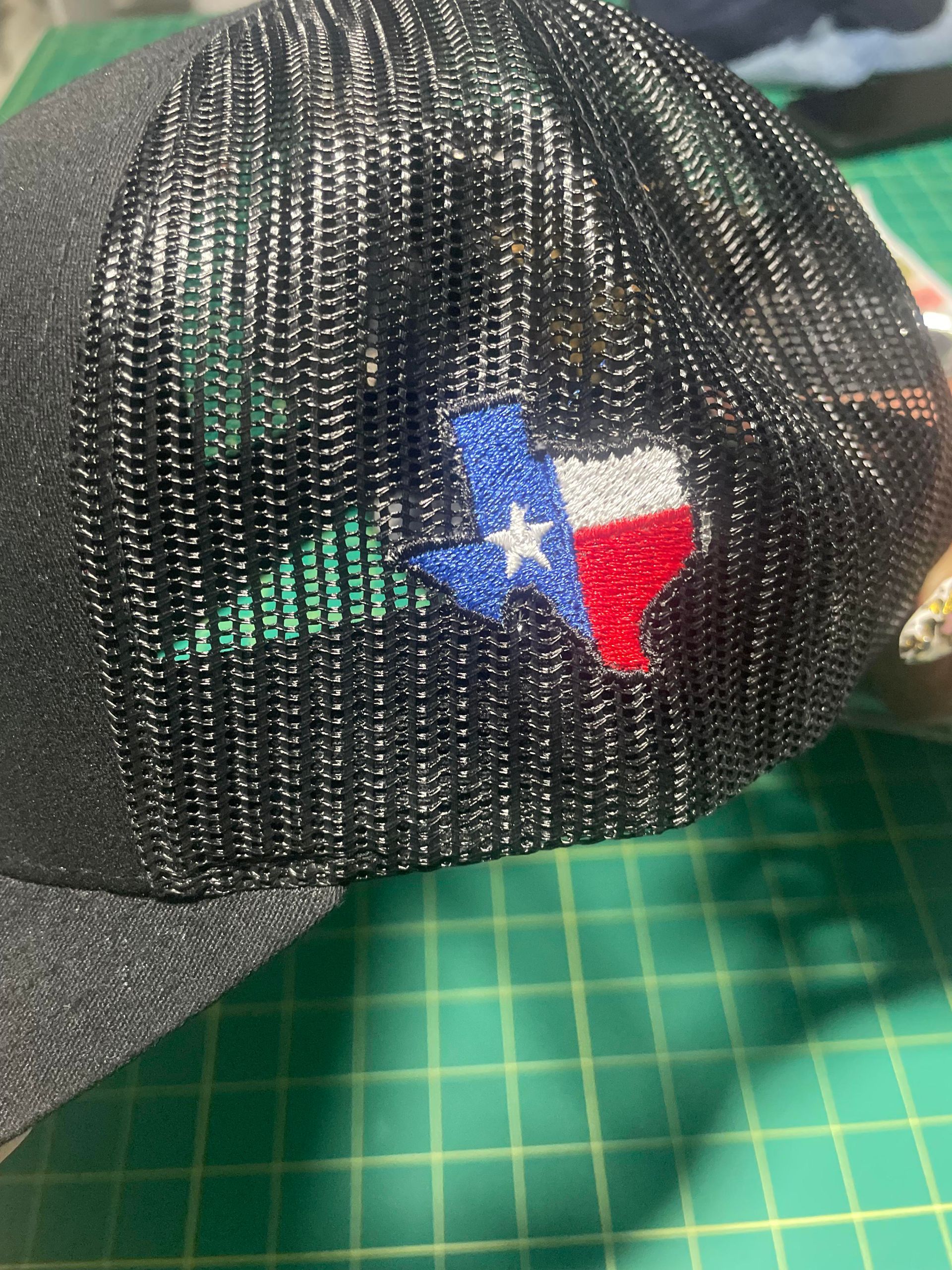 Black mesh cap with a Texas flag patch on a green cutting mat.