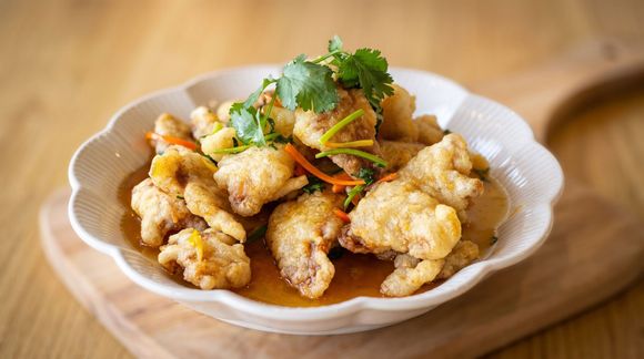 Plate of golden fried chicken pieces topped with herbs and shredded vegetables on a wooden board