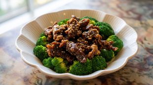 Broccoli florets topped with glossy beef on a white scalloped plate