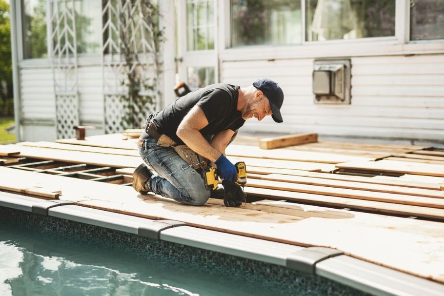 Worker kneeling on a wooden pool deck, using tools beside the water