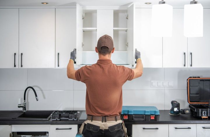 Person in a kitchen opening white cabinet doors above a sink and stove.