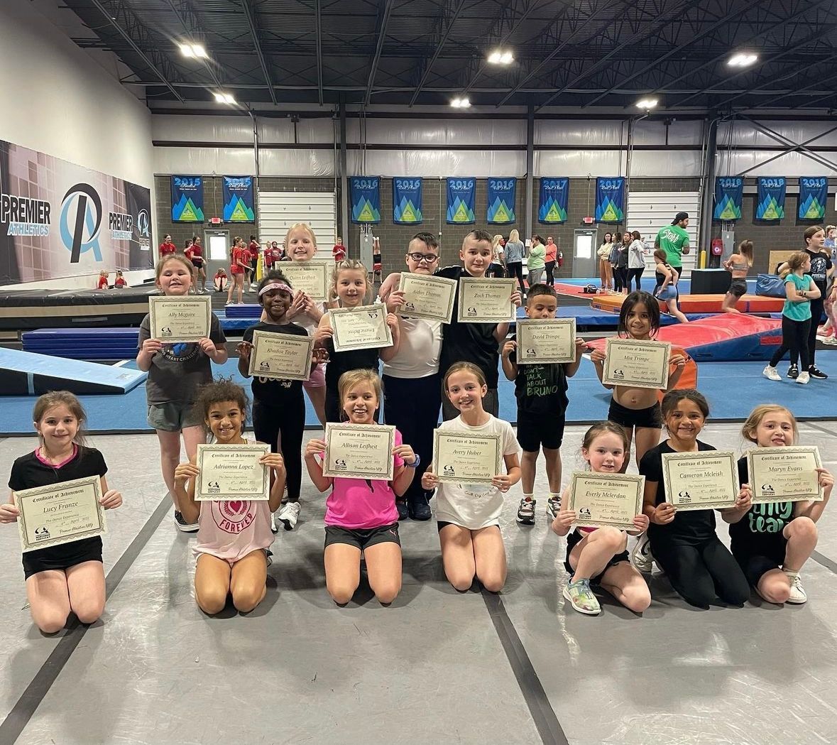 A group of children are posing for a picture in a gym holding certificates.