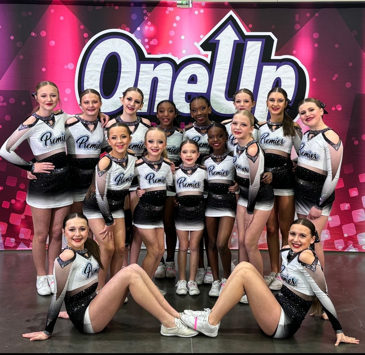 A group of cheerleaders are posing for a picture in front of a oneth banner.