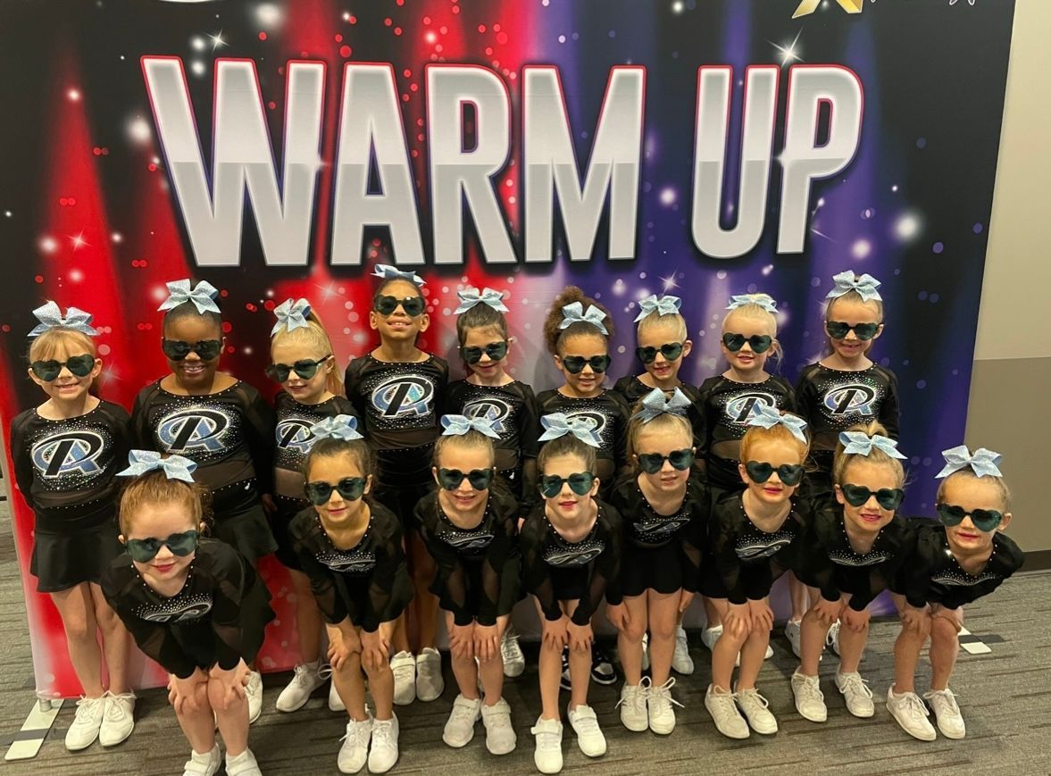 A group of cheerleaders are posing for a picture in front of a sign that says warm up.