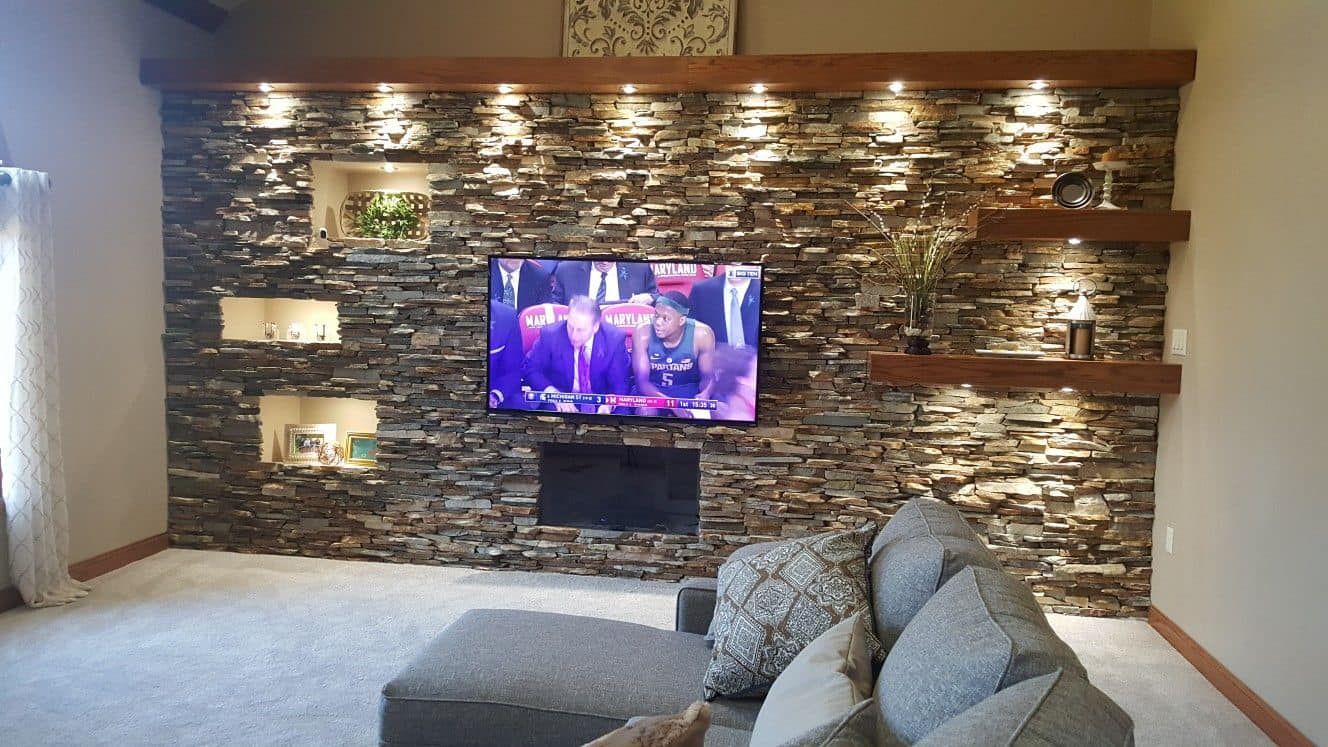 Living room with stacked-stone accent wall, mounted TV, and gray sectional sofa