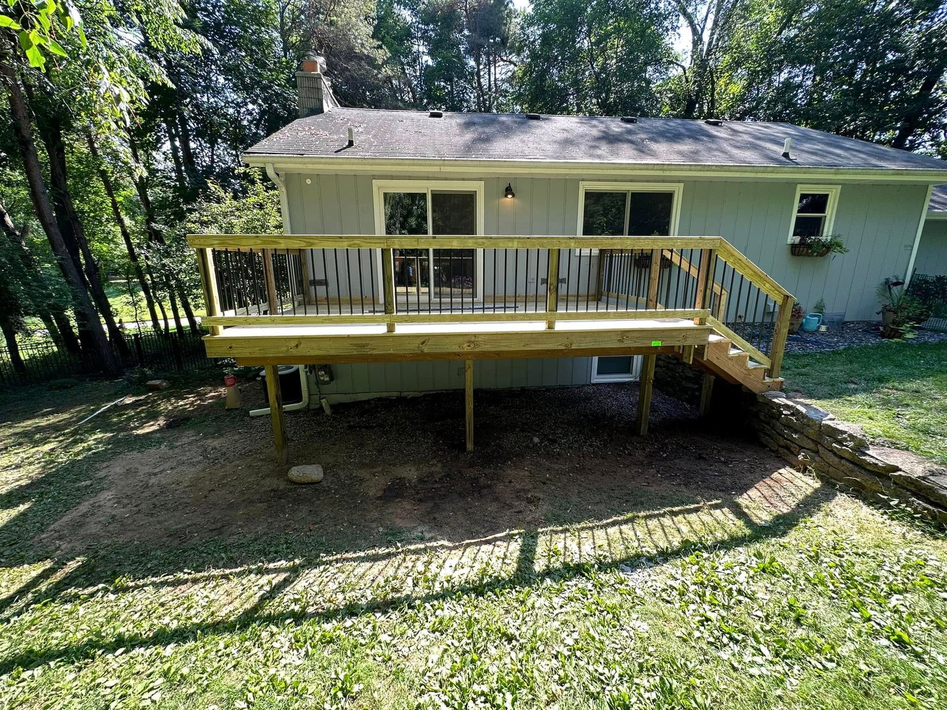 Yellow wooden deck attached to a light green house in a wooded backyard