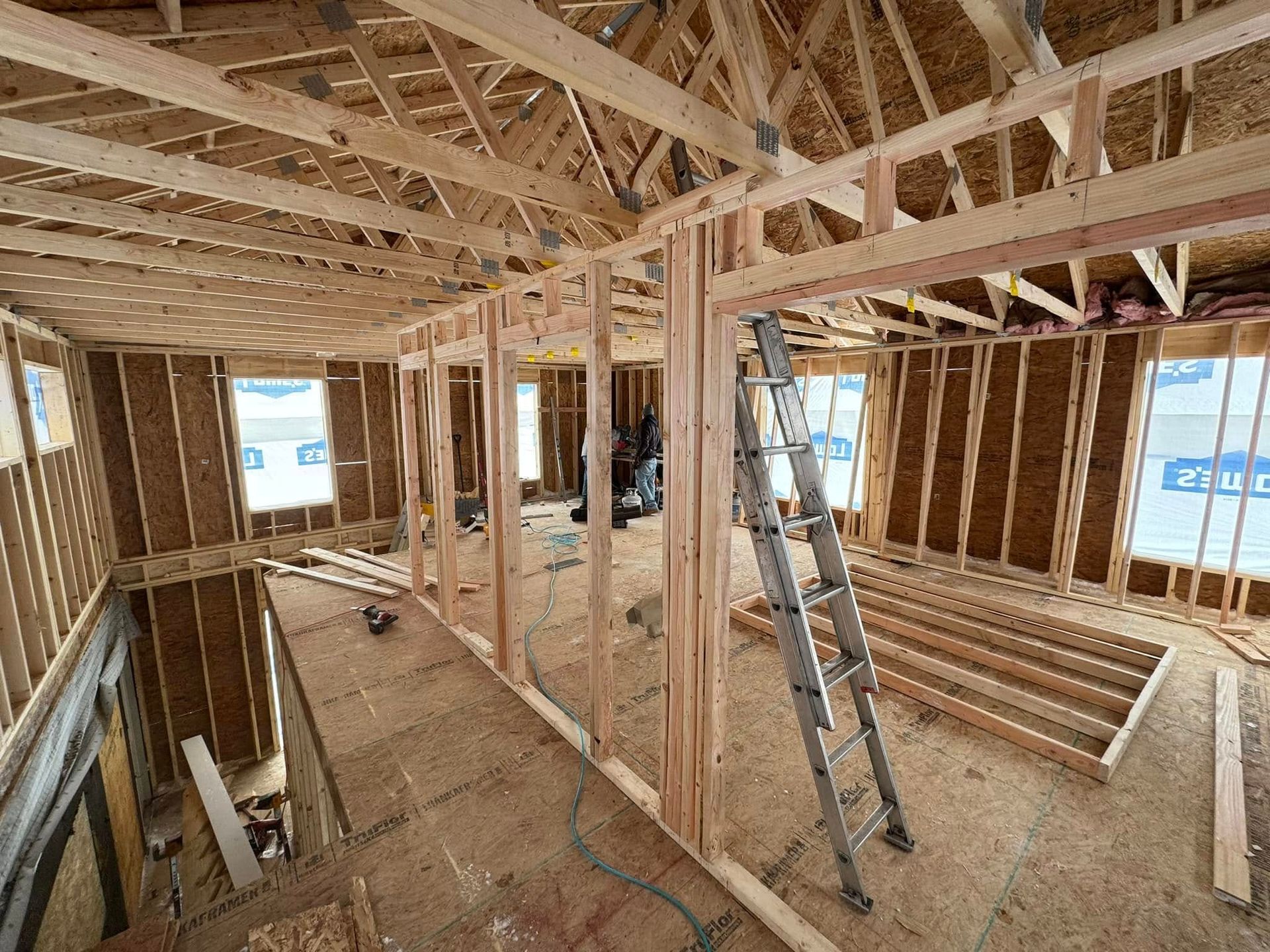 Interior of a house under construction with exposed wooden framing and a ladder in the center.