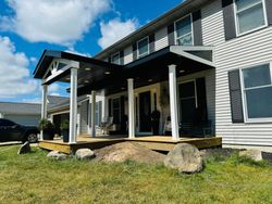 Two-story gray house with a covered porch, black shutters, and a grassy yard with large rocks