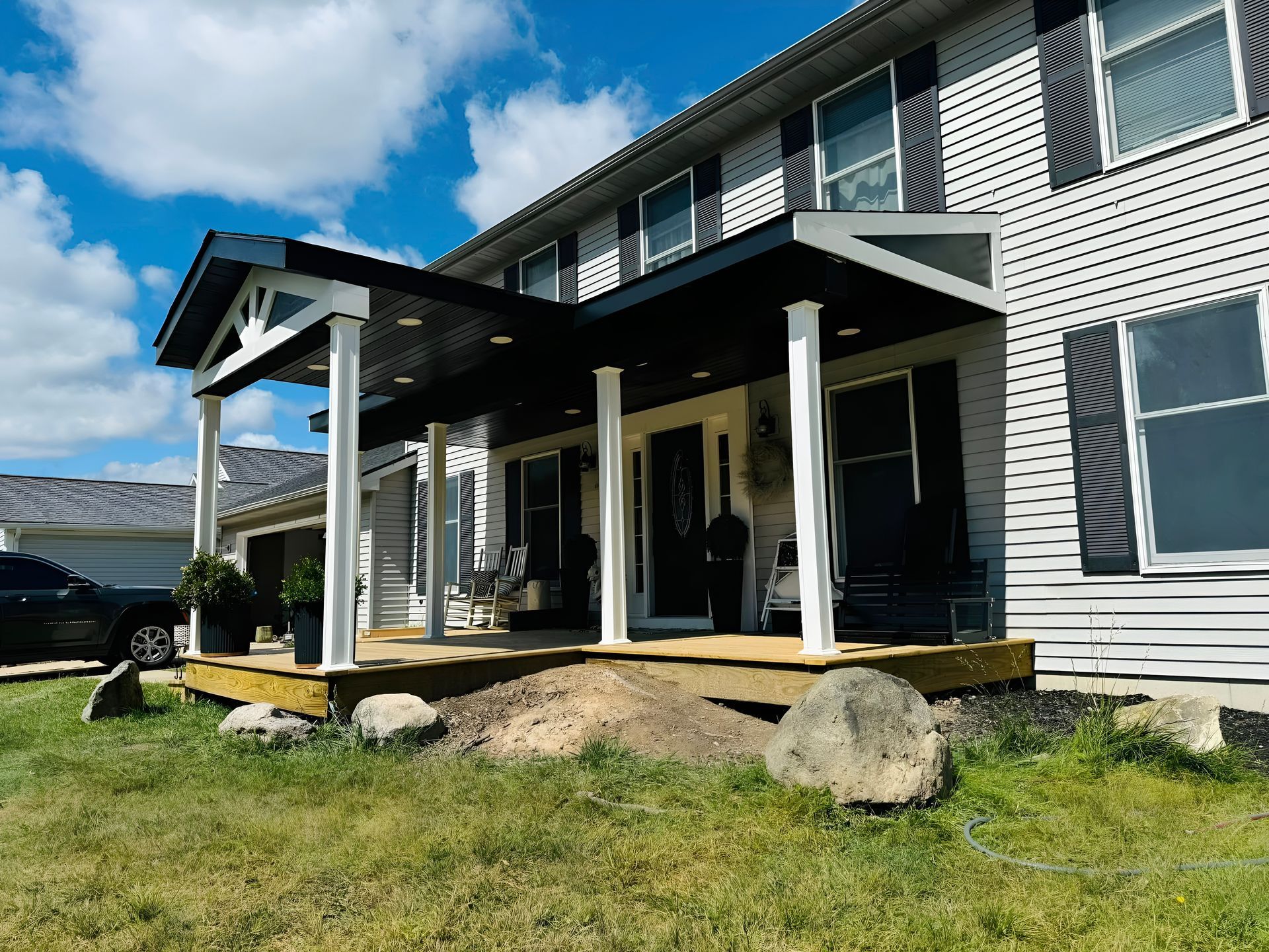 Two-story house with a covered front porch, gray siding, and stone landscaping in a grassy yard