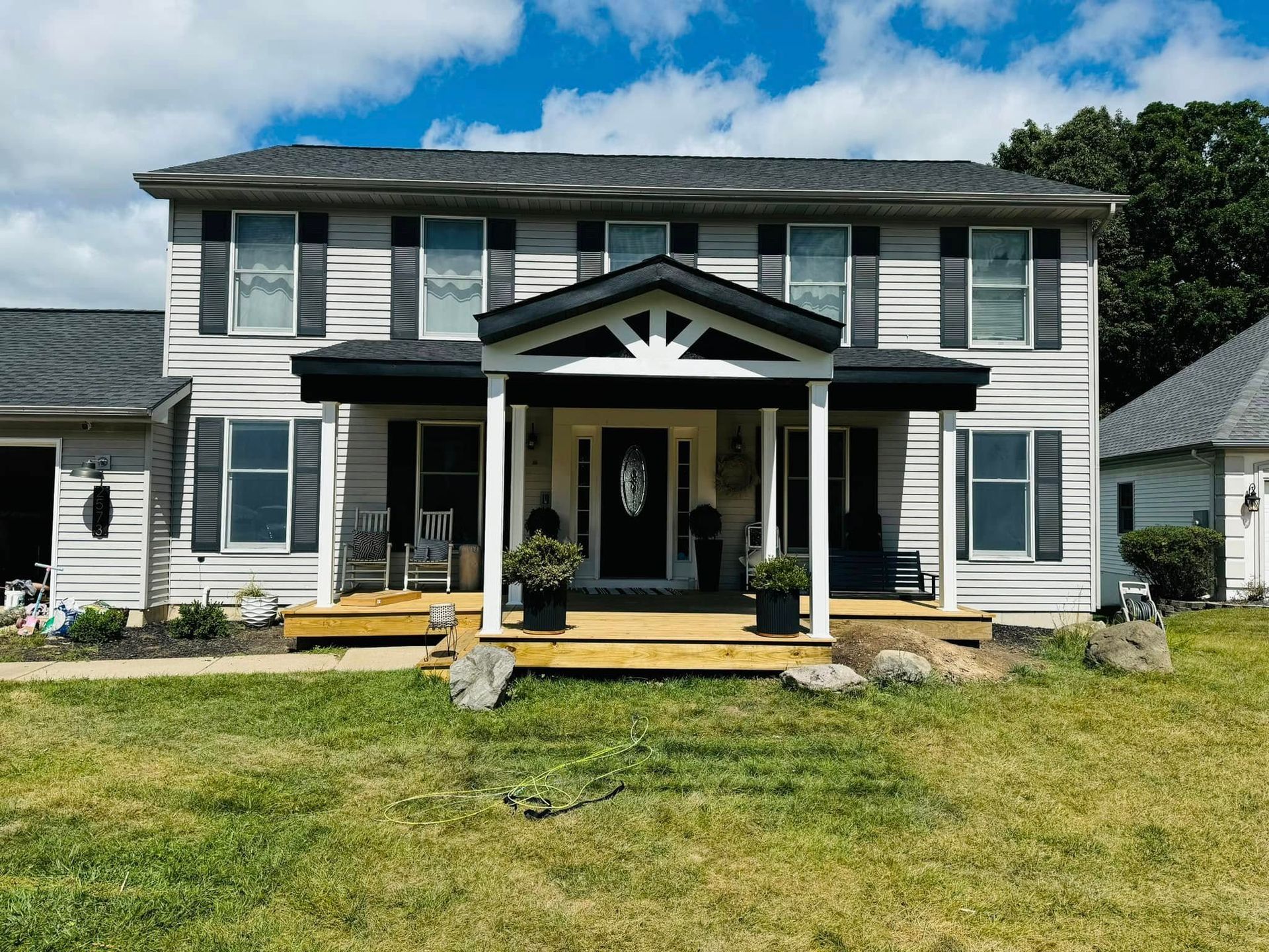 White two-story house with black shutters and porch, fronted by a lawn under a blue sky.