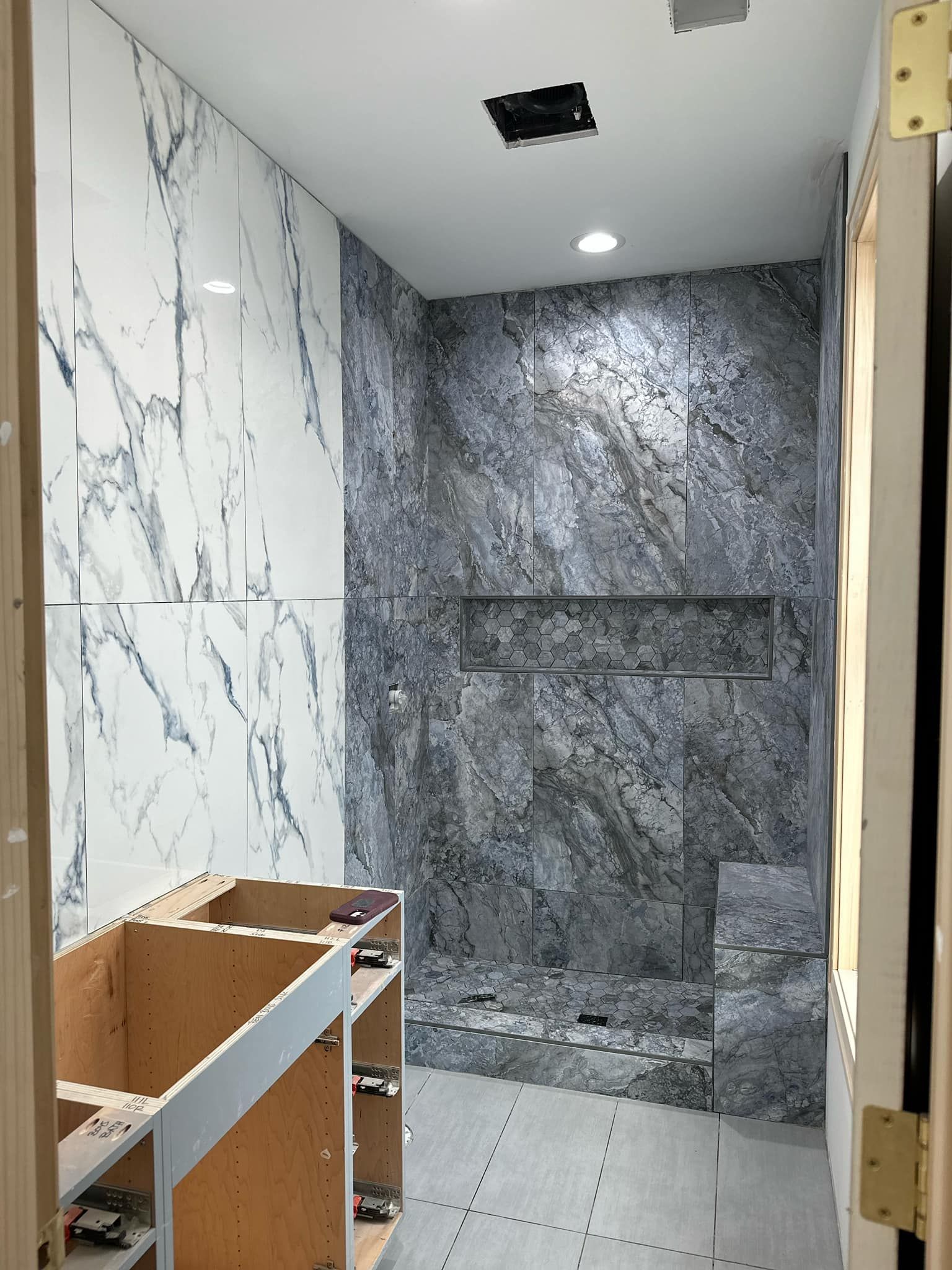 Narrow hallway with marble-look walls, a gray tiled back wall, and an unfinished cabinet in the foreground