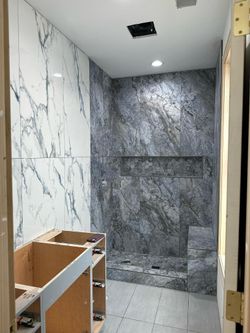 Narrow hallway with marble-look walls, a gray tiled back wall, and an unfinished cabinet in the foreground