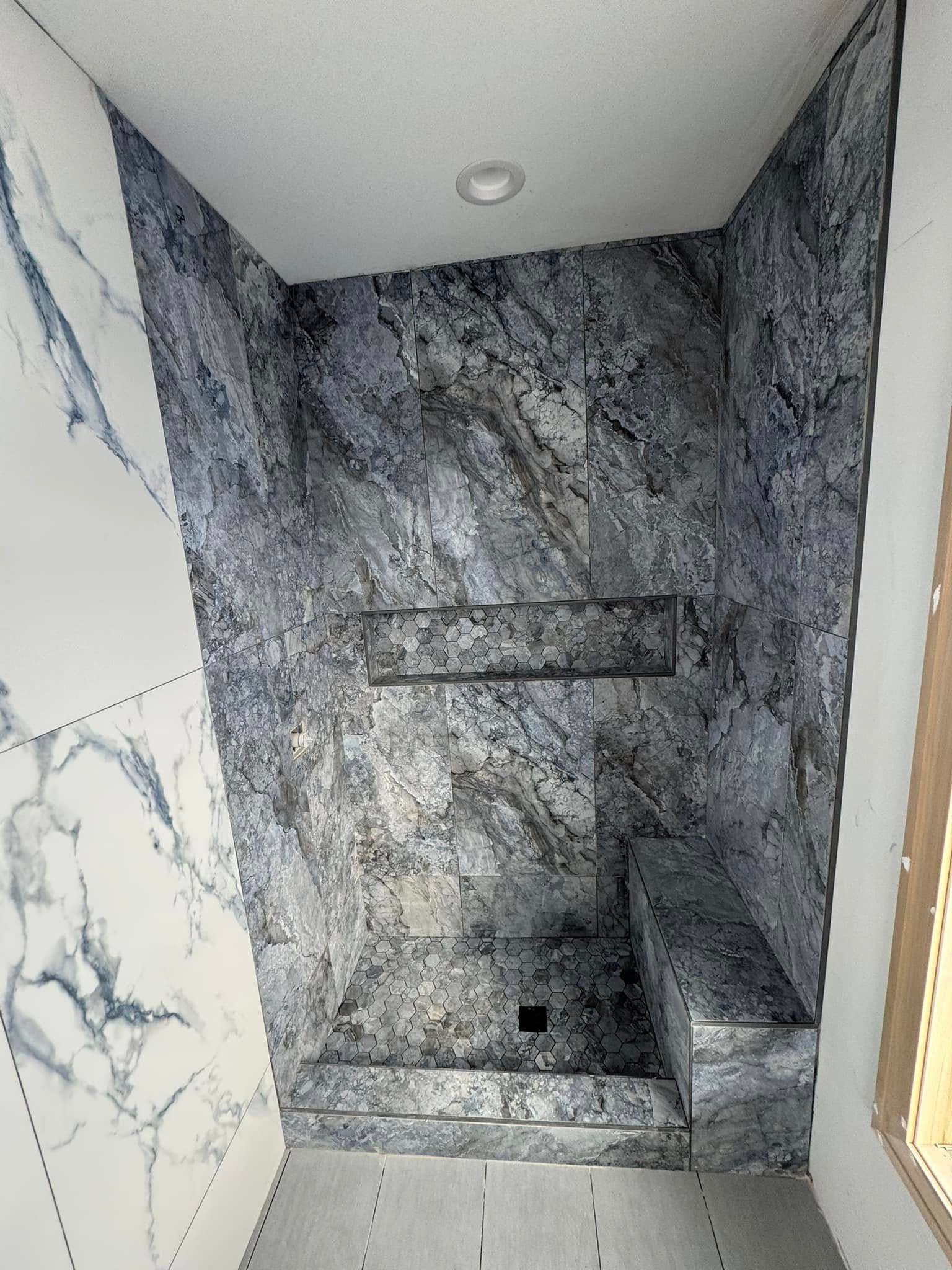Empty gray stone shower niche with a built-in bench and recessed ceiling light