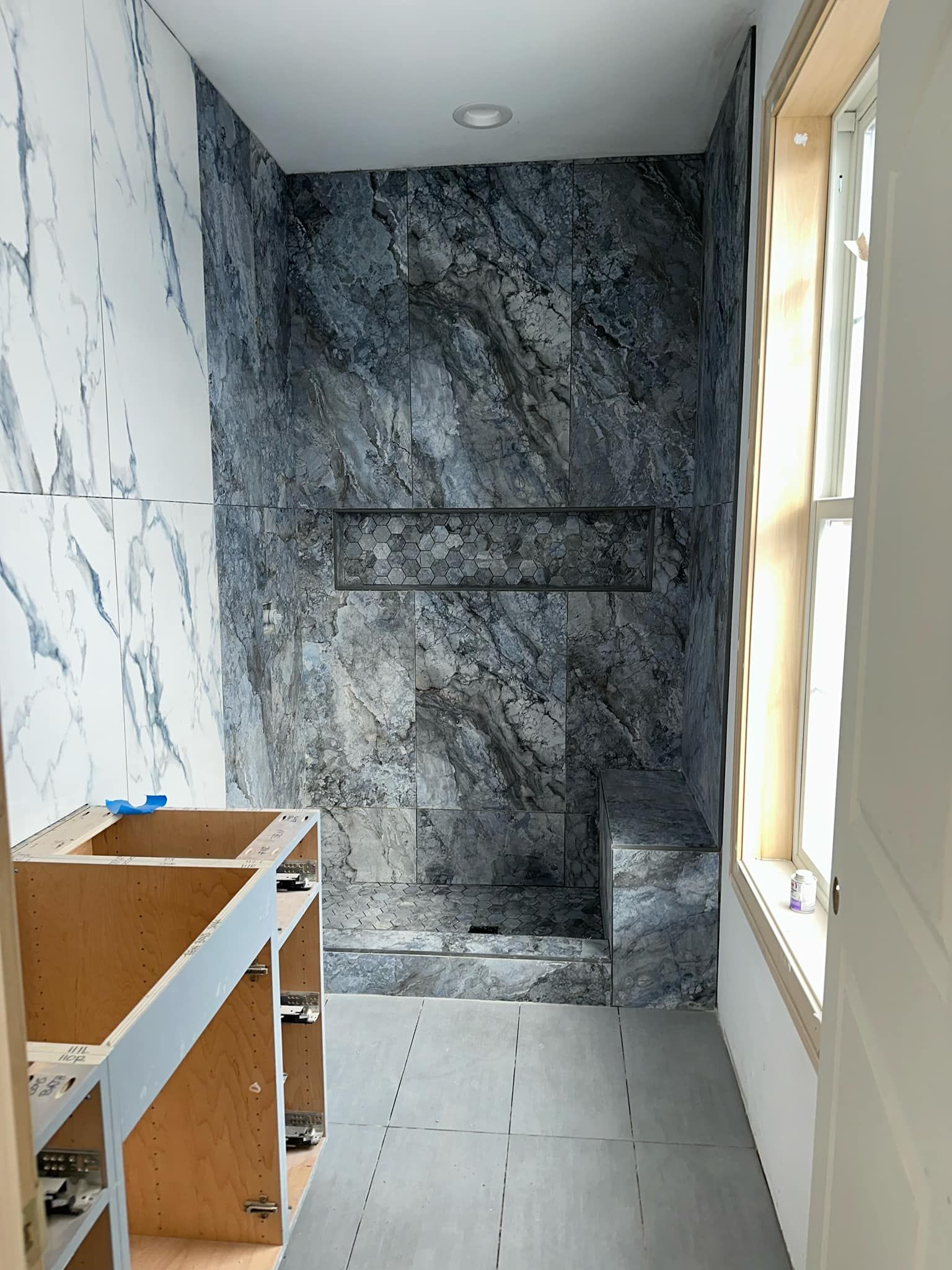 Small bathroom under renovation with marble-pattern walls, unfinished vanity, and a window.