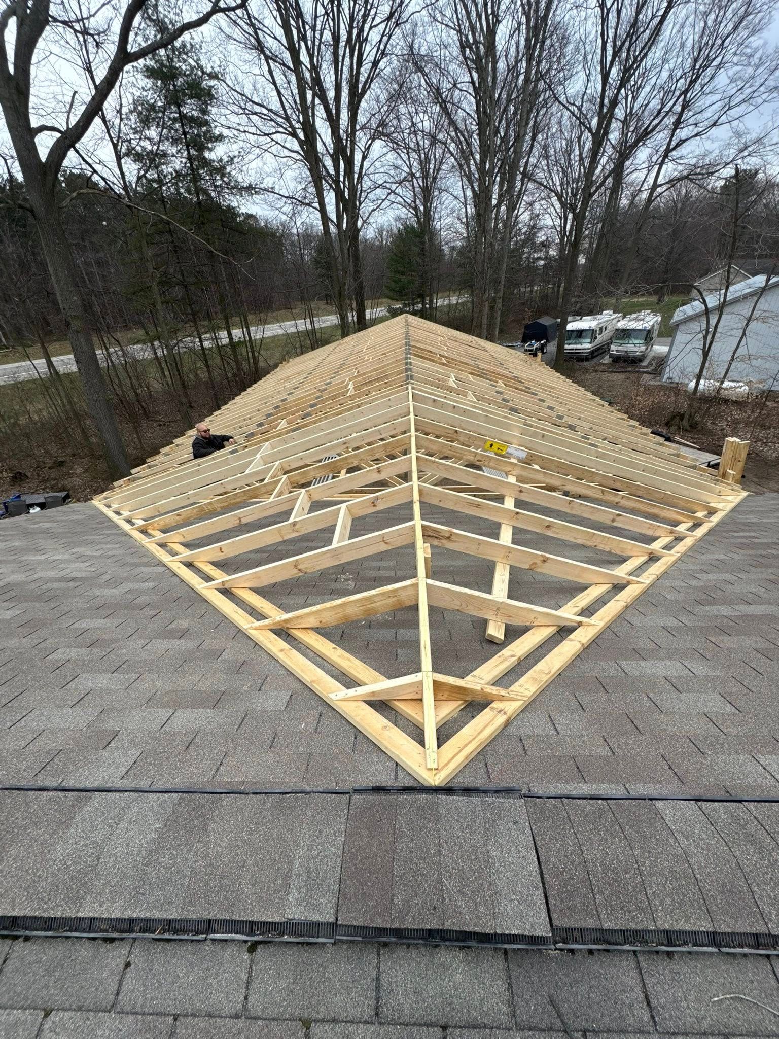 Rooftop framing under construction with wooden trusses on a building in a wooded area