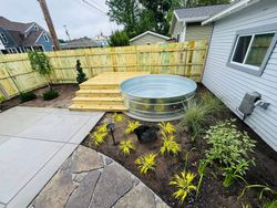 Backyard garden with raised wooden steps, metal water feature, and newly planted shrubs beside a house