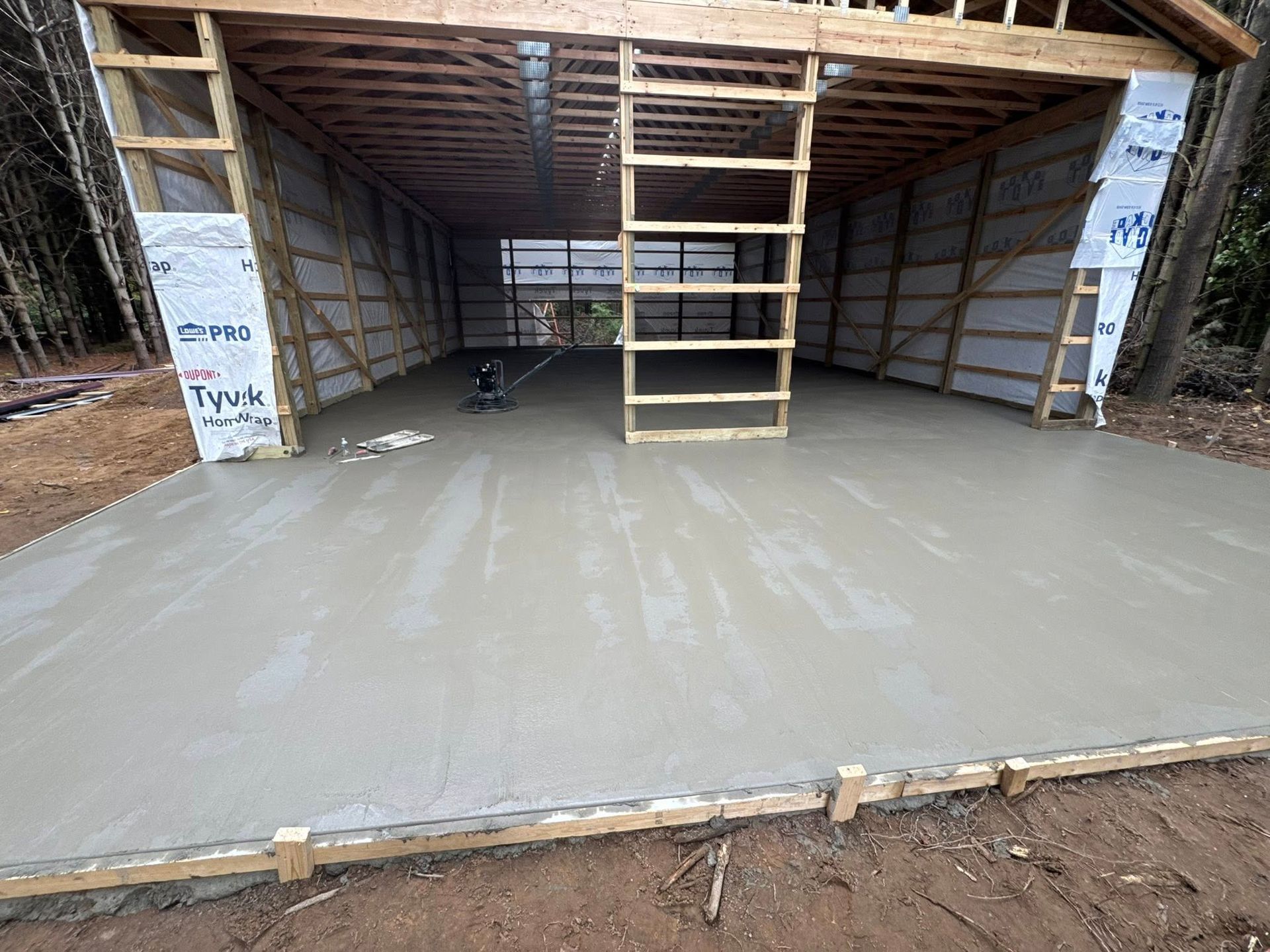 Freshly poured concrete floor inside an open-sided wooden shed under construction.