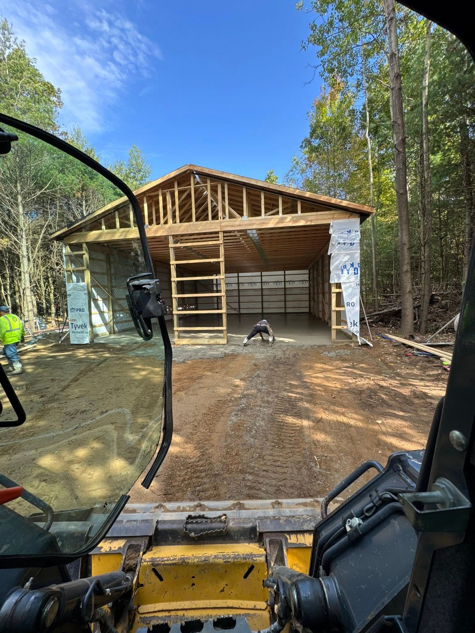 View from a construction vehicle facing a house under renovation with exposed framing and a ladder.