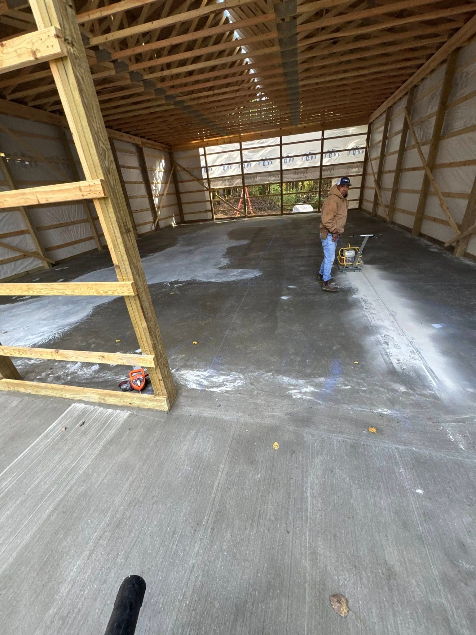 Large unfinished garage interior with a person standing on a concrete floor beneath exposed wooden rafters.