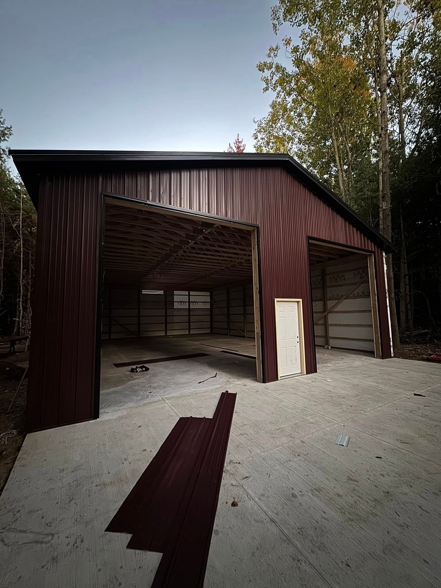 Rustic barn with open doors and weathered red siding on a gravel lot surrounded by trees.