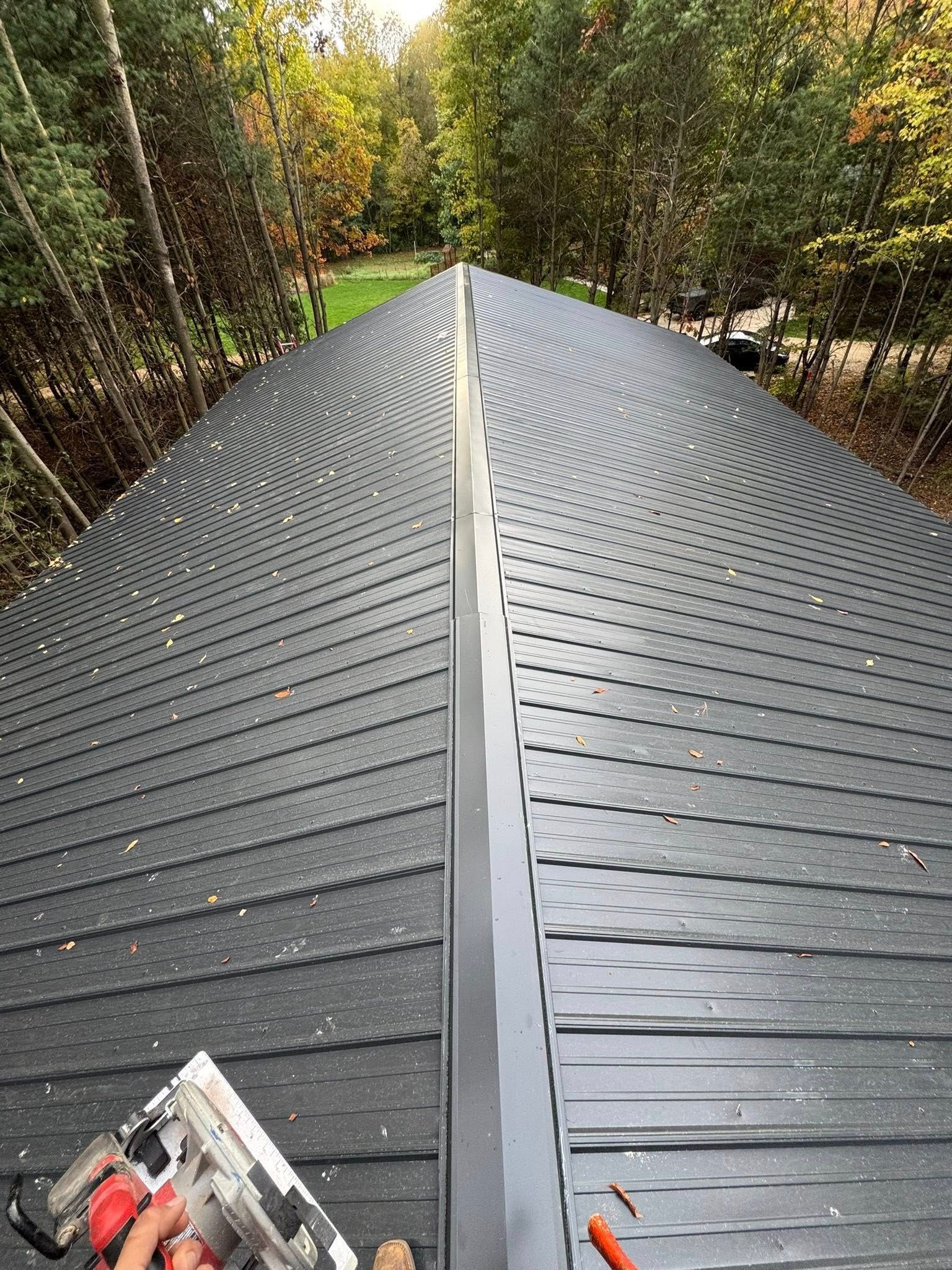 Curved black metal roof walkway through a wooded area, with a chainsaw at the lower left.