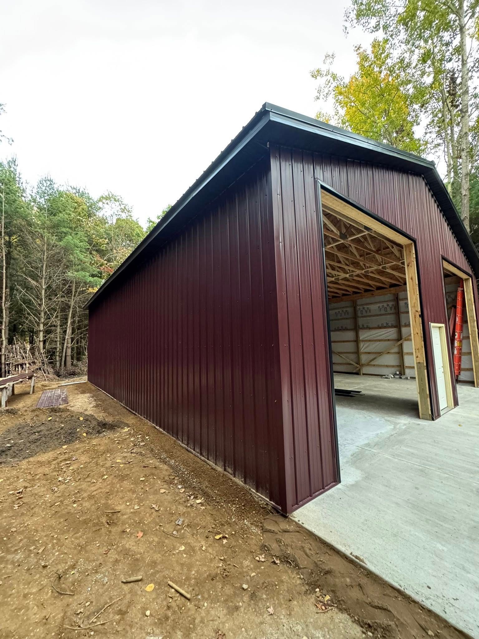 Maroon metal shed with open front on a concrete pad beside a wooded area