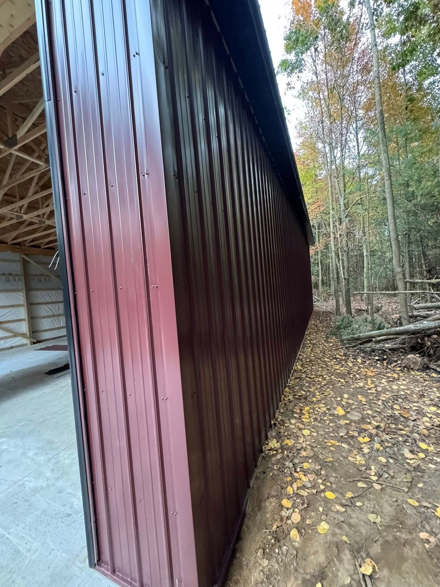 Wooden building corner with maroon siding beside a gravel path and leafy forest groundcover.