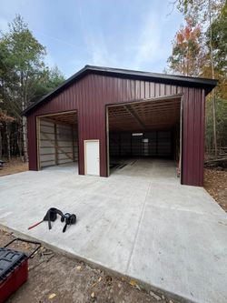 Maroon metal garage with two open bays and a white side door on a gravel driveway.