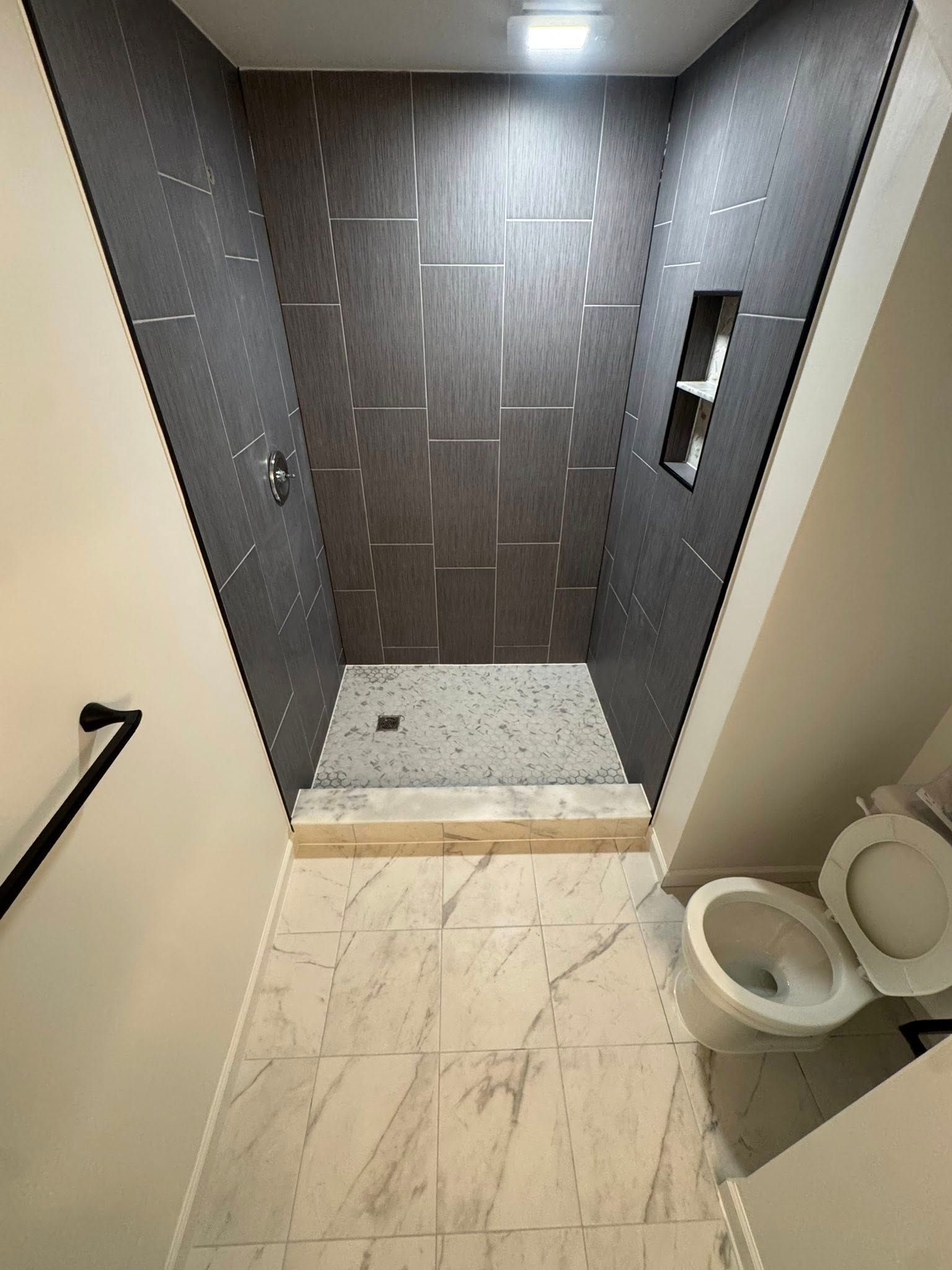 Walk-in shower with dark gray tile, white floor, and nearby toilet in a bathroom.