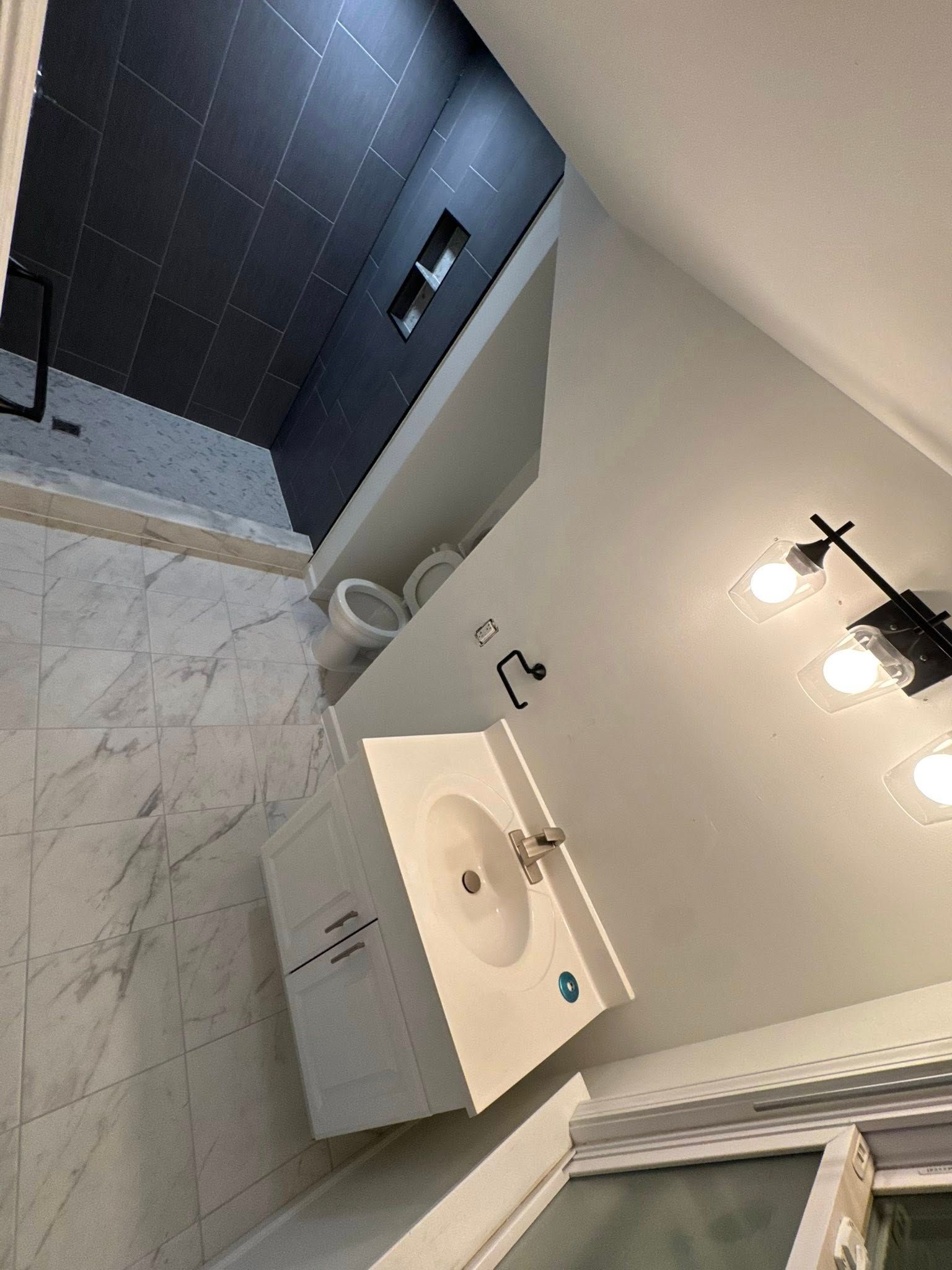 Small bathroom with white sink vanity, mirror, wall lights, and tiled shower area.
