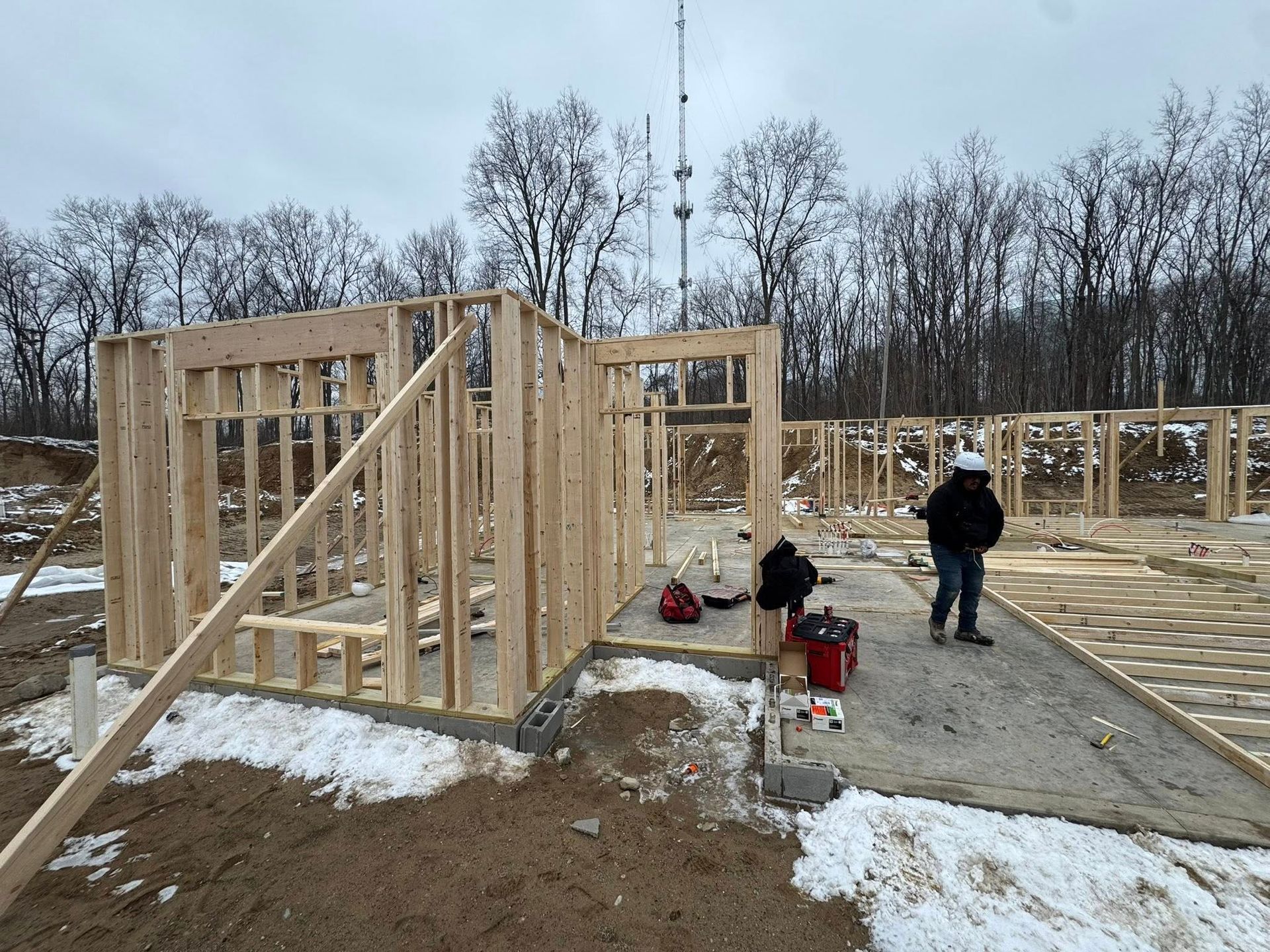 House framing construction site with workers, bare wooden walls, and patches of snow on the ground
