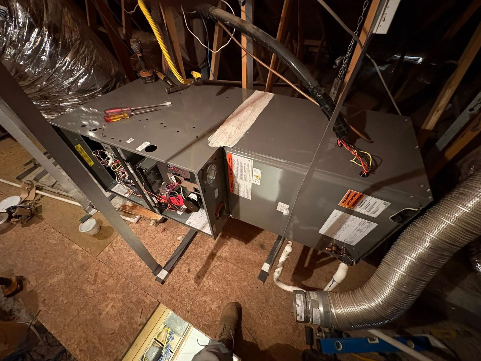 Furnace and ductwork in a cramped attic crawlspace, with exposed wiring and insulation.