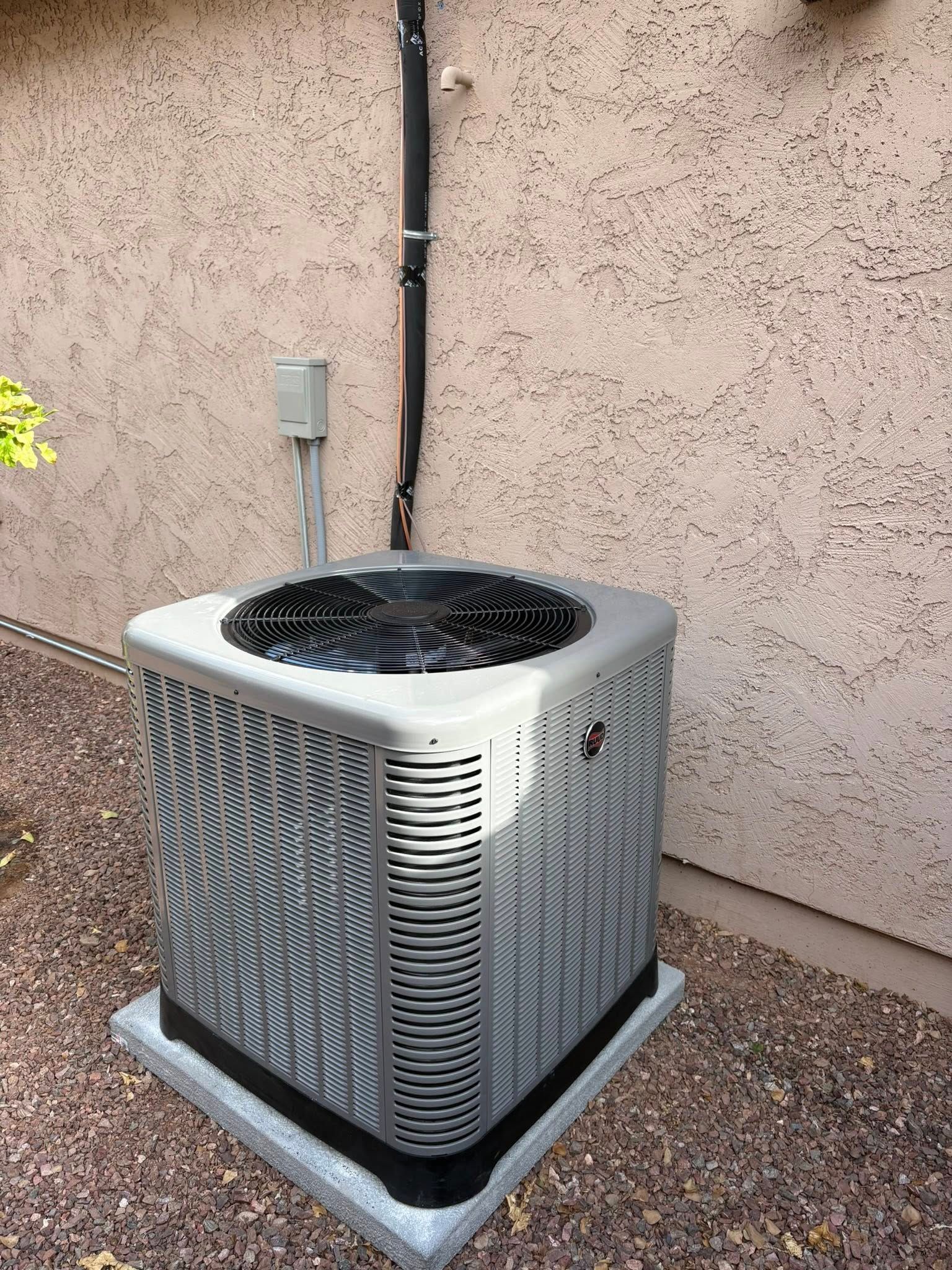 Outdoor air conditioner unit beside a stucco wall with a black pipe above it