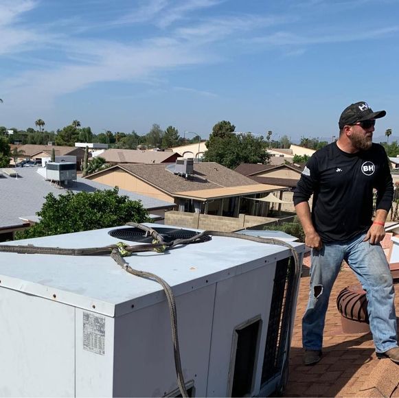 Technician standing on a rooftop beside a large HVAC unit under a clear blue sky