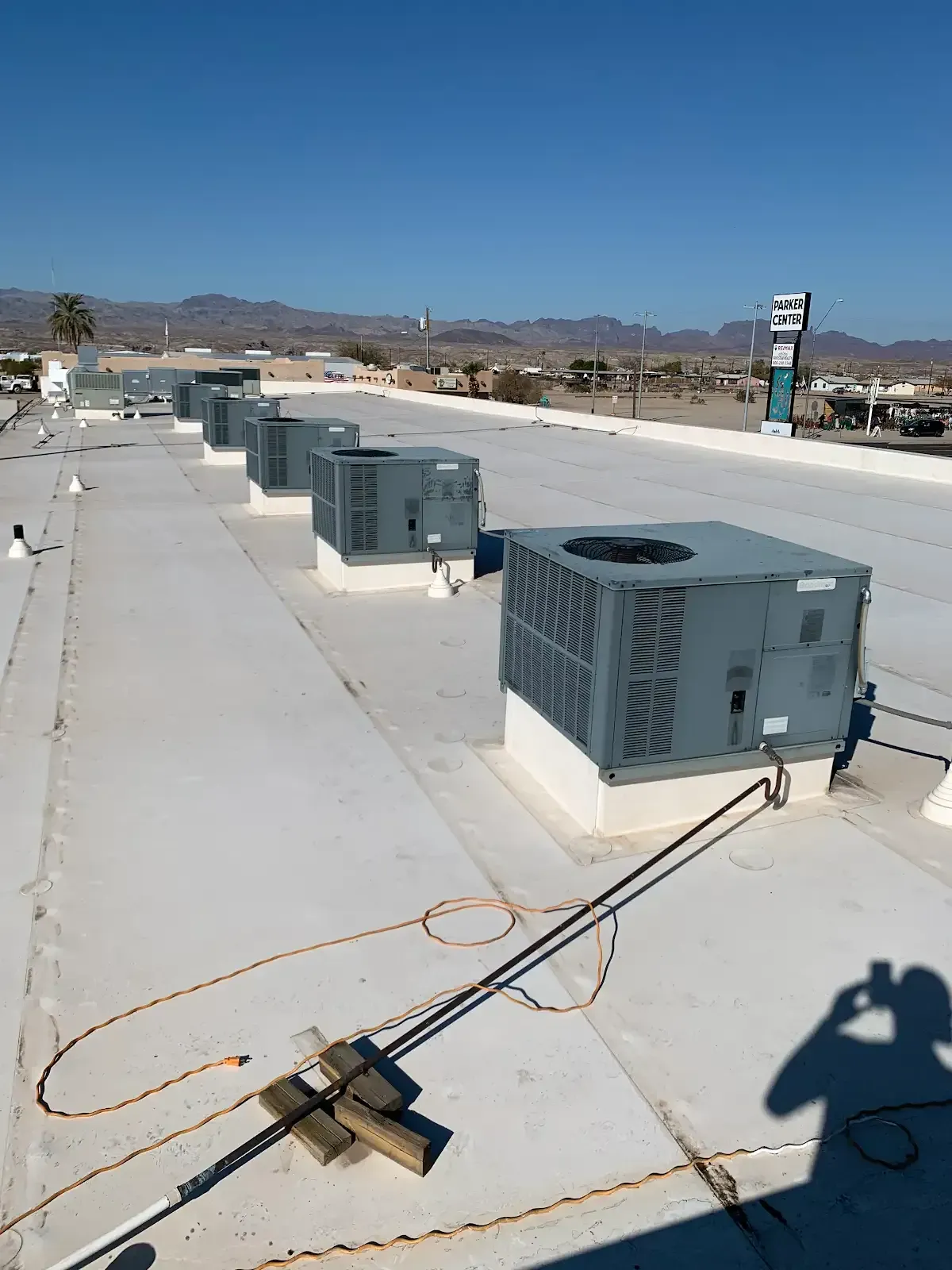 Rooftop HVAC units lined on a flat roof under a clear blue sky, with distant mountains and a utility pole.