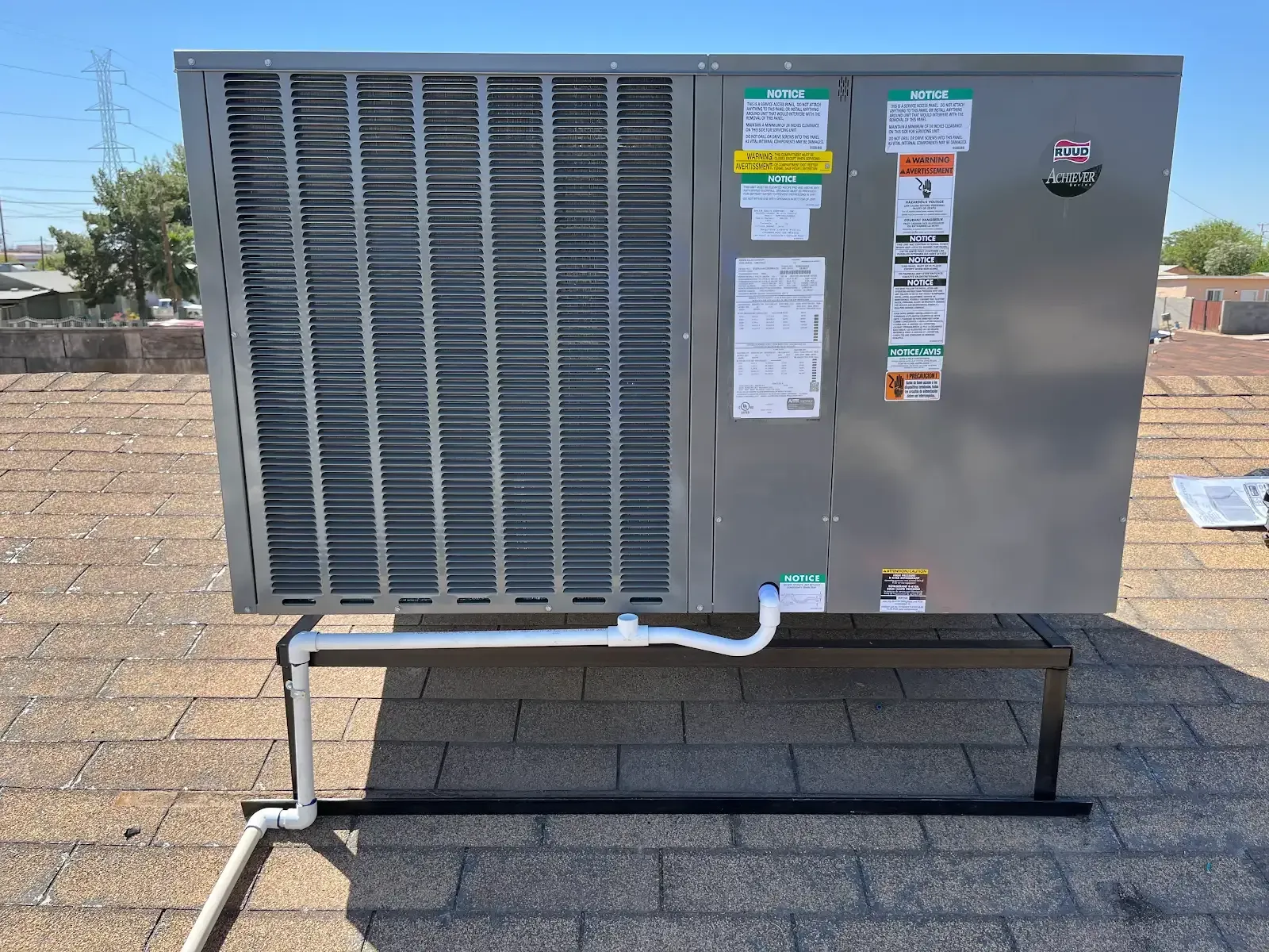 Outdoor HVAC condenser unit on a raised metal stand in a gravel yard, with warning labels on the front.