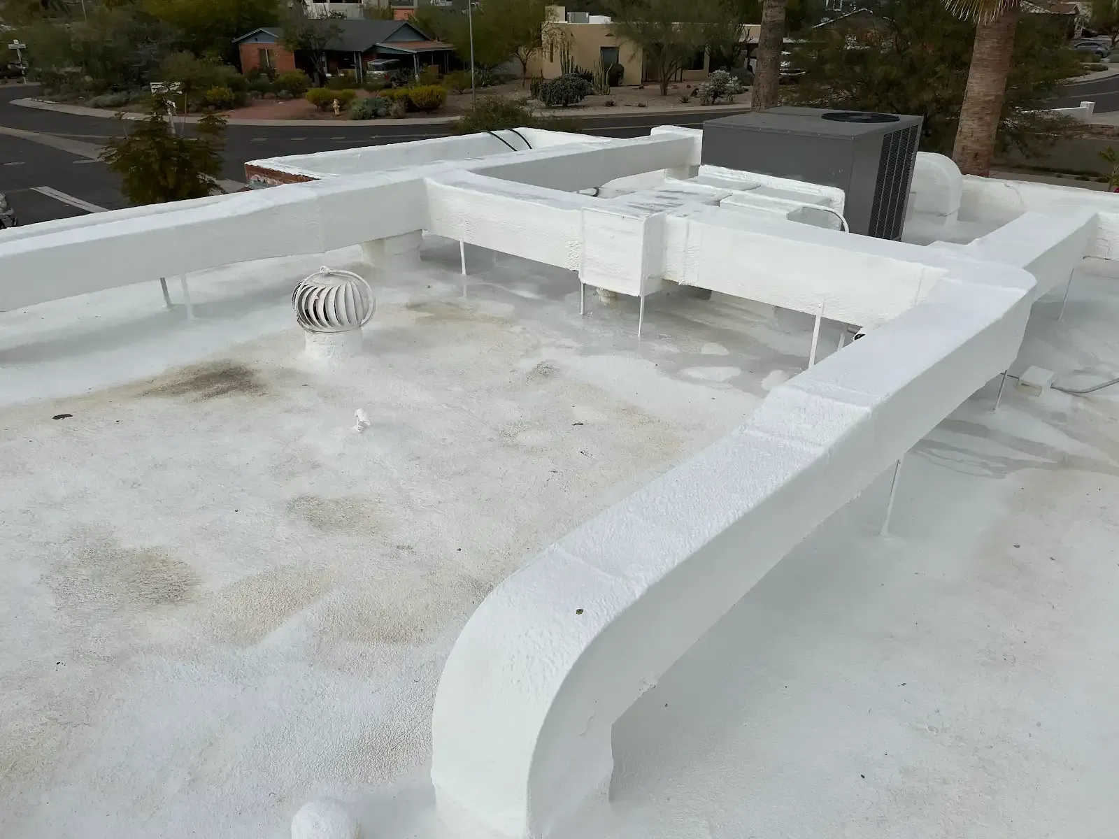 White rooftop with low HVAC ducting and a vent, overlooking houses and trees behind.