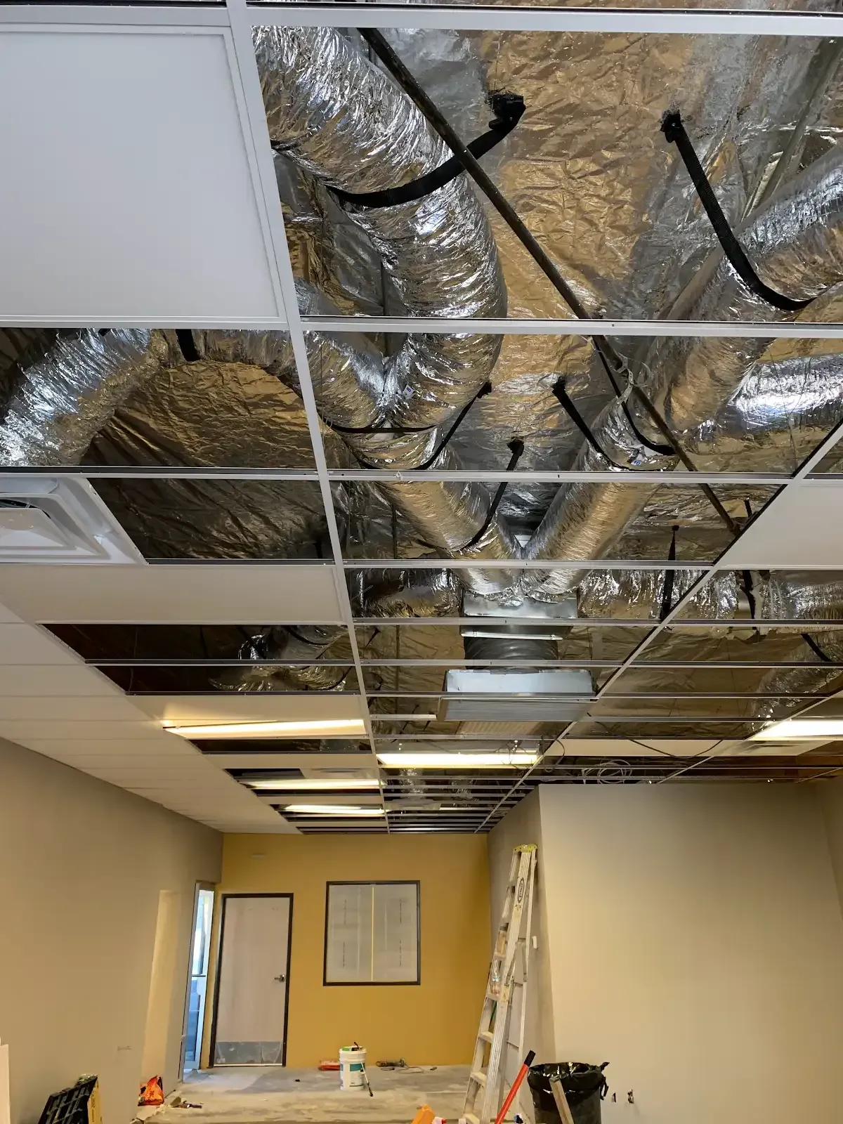 Office under construction with exposed ceiling ducts, missing tiles, and a partially finished room.