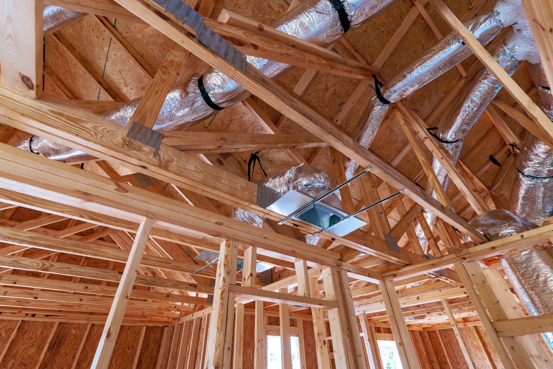 Wood-framed house roof under construction, with exposed trusses and blue insulation panels.