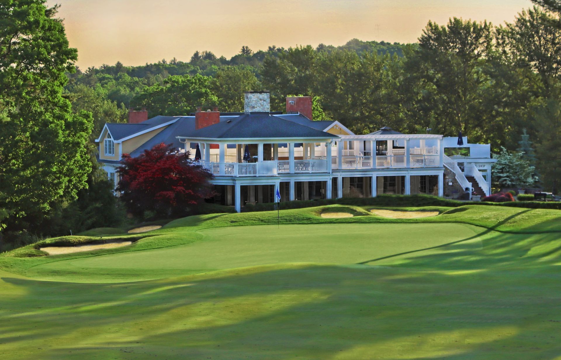 A large white house is sitting on top of a green hill next to a golf course.